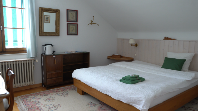 The room is furnished with a rug, a bed and a chest of drawers.