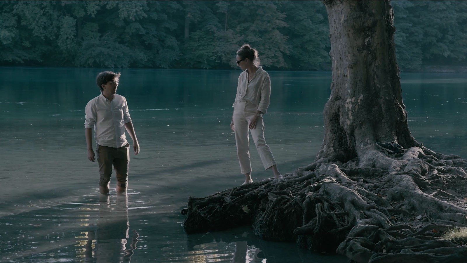 Two people standing by the river looking at each other.