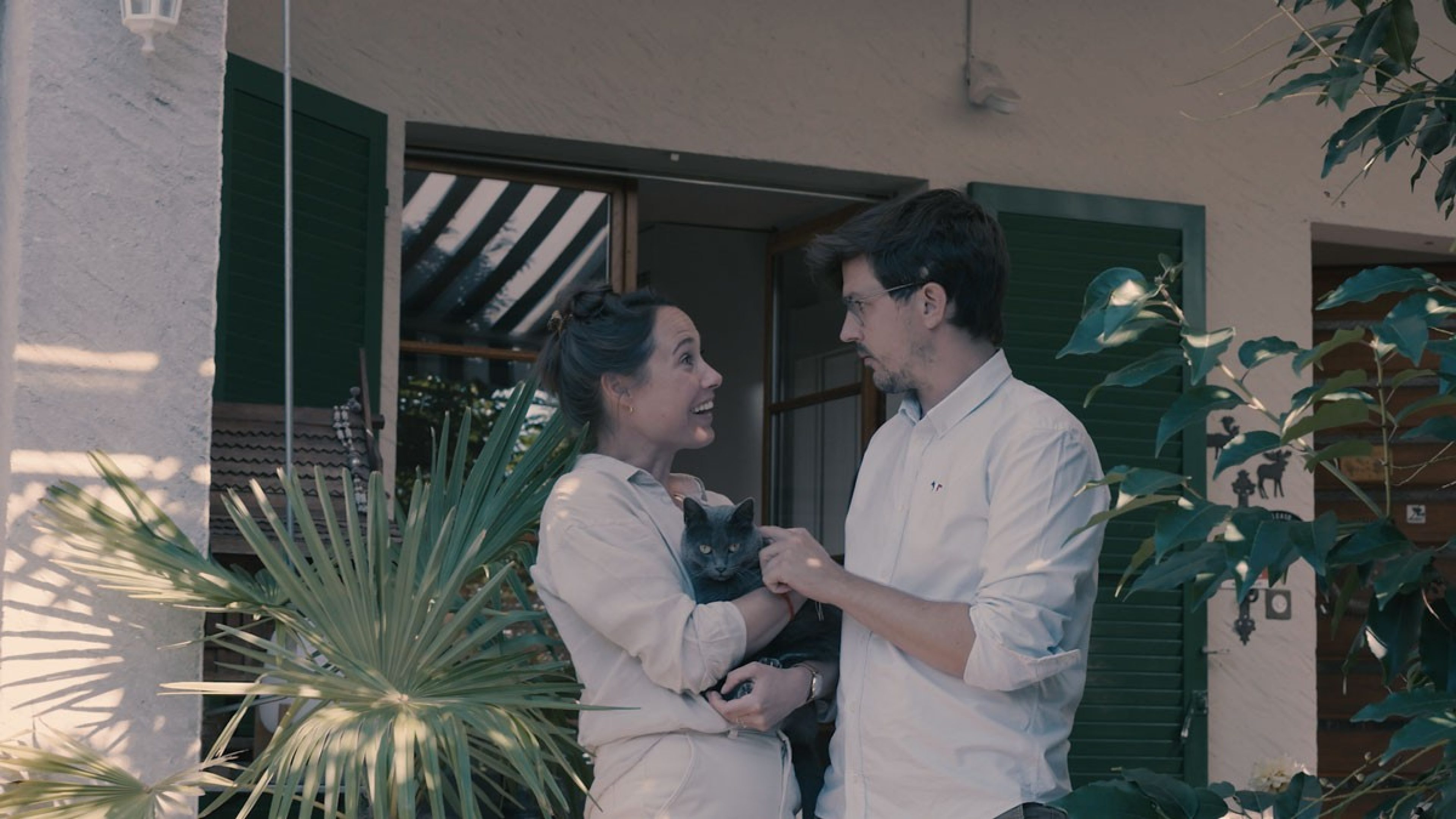 A couple holding a cat standing in front of a house