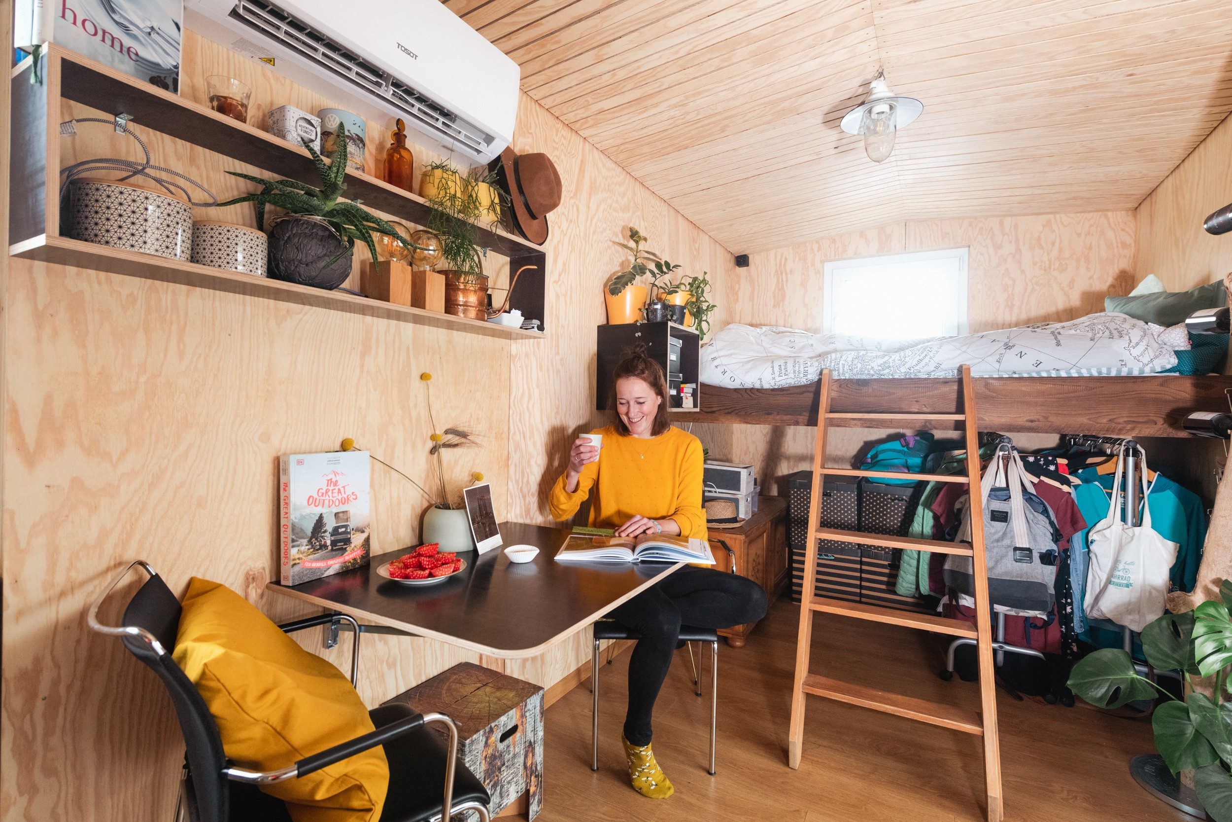 A woman sits in a shipping container house drinking coffee