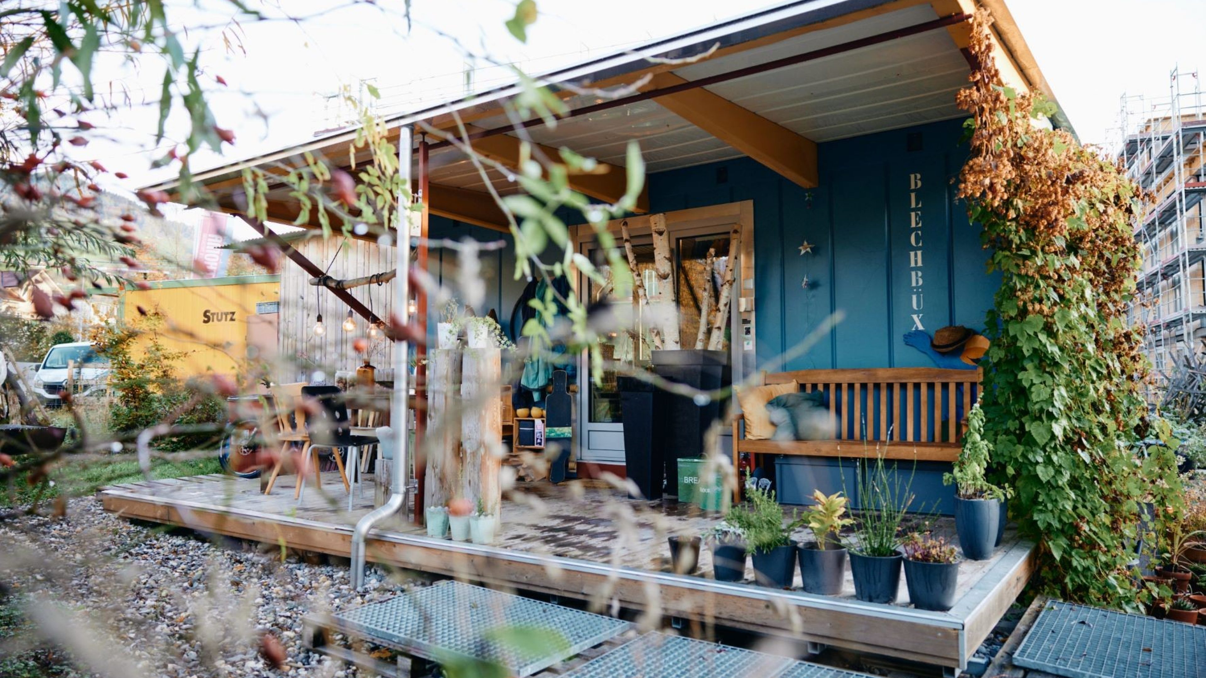 A shipping container house with plants growing on it and the inscription “Blechbüx” (tin can)