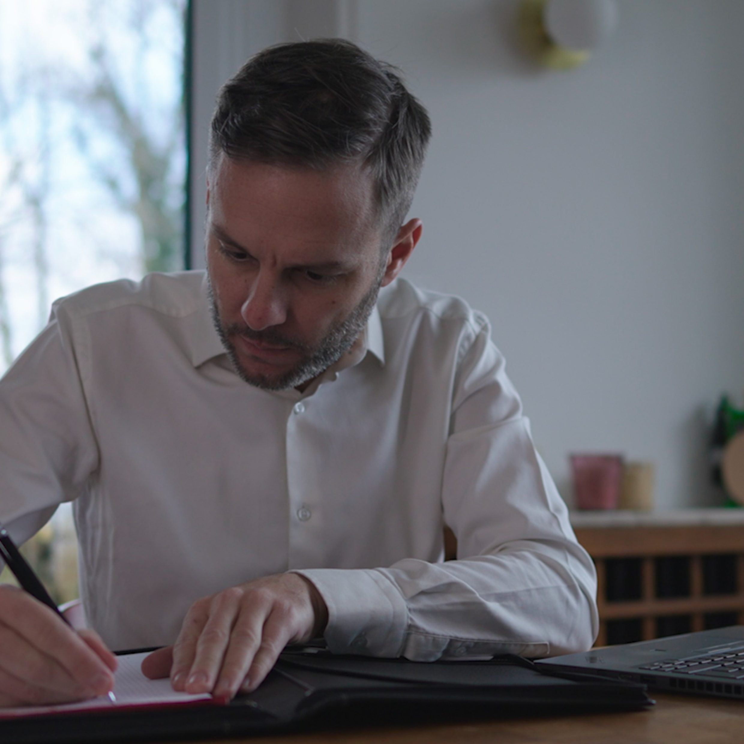 A man in a business outfit writing on a notepad.