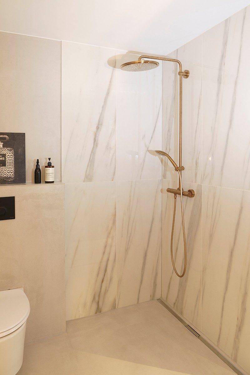 A shower with marble tops and gold fittings.