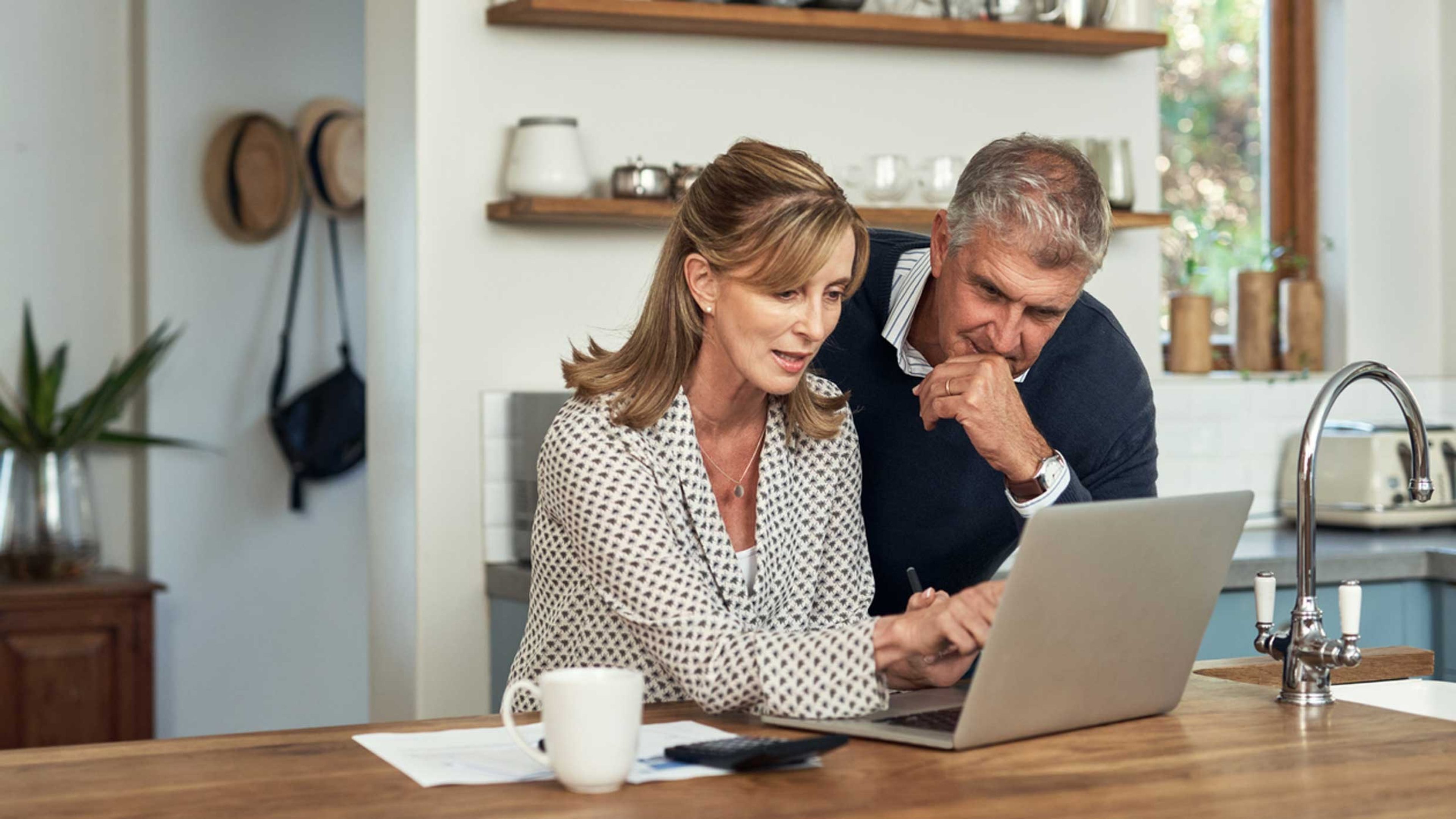 A couple look at a laptop while making a calculation.