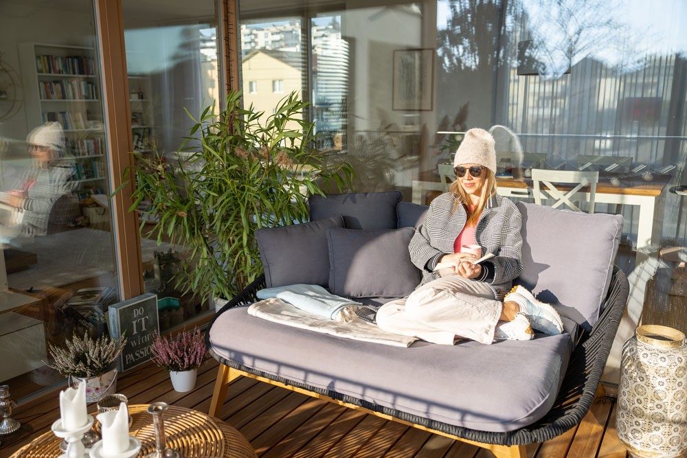 A woman sits on an outdoor sofa on a loggia.