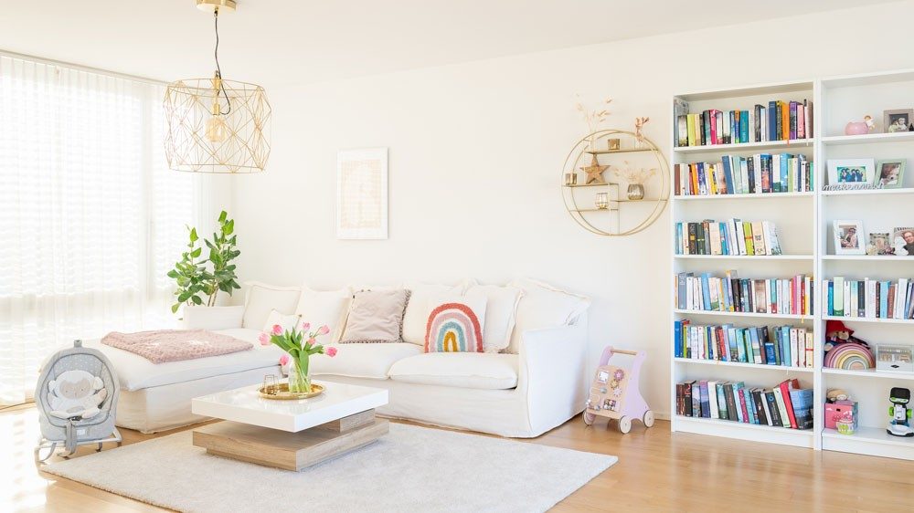 A living room with a white sofa with toys and a shelf full of books next to it. 