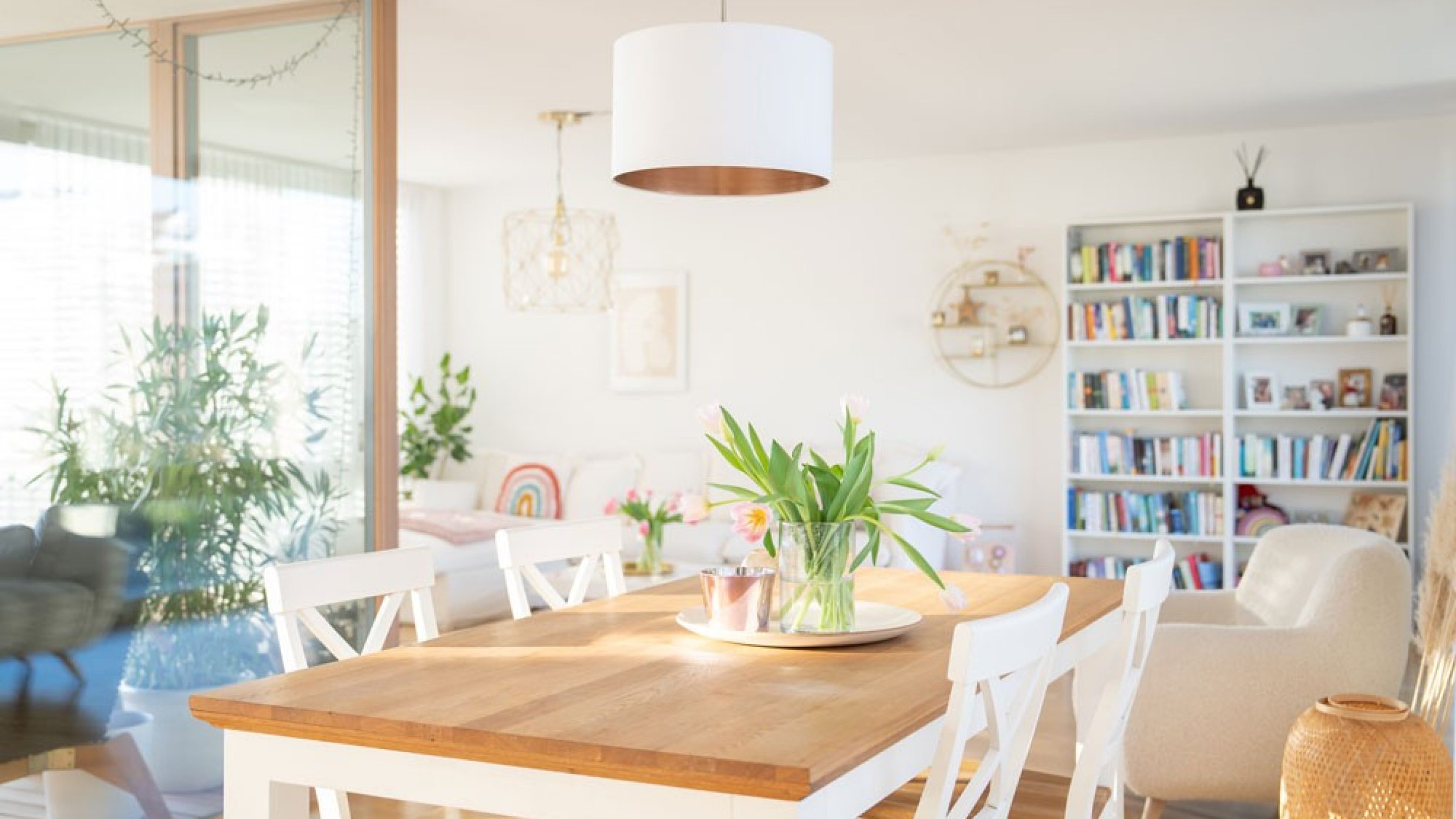 A dining table with beautiful tulips, behind which is a view of the loggia and the living room with a bookshelf.