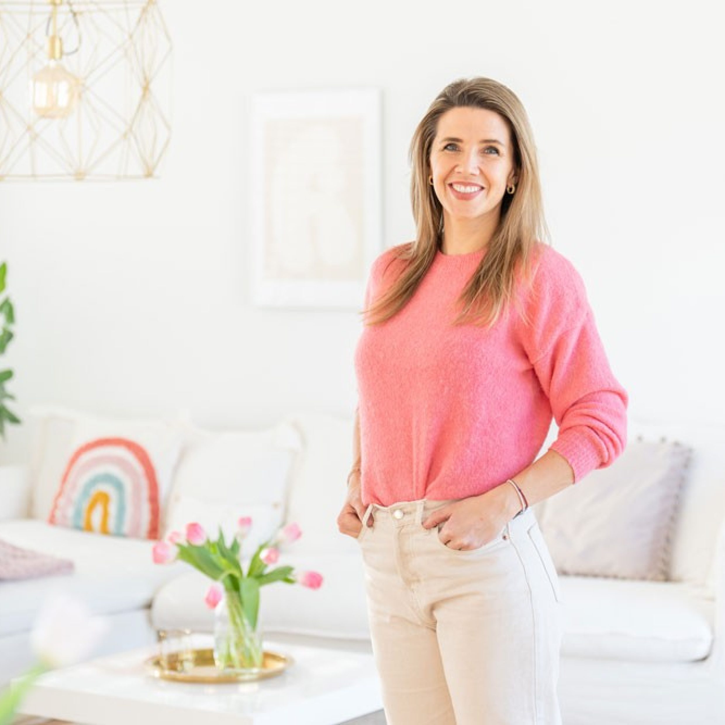 A woman in a pink sweater stands in front of a sofa. 