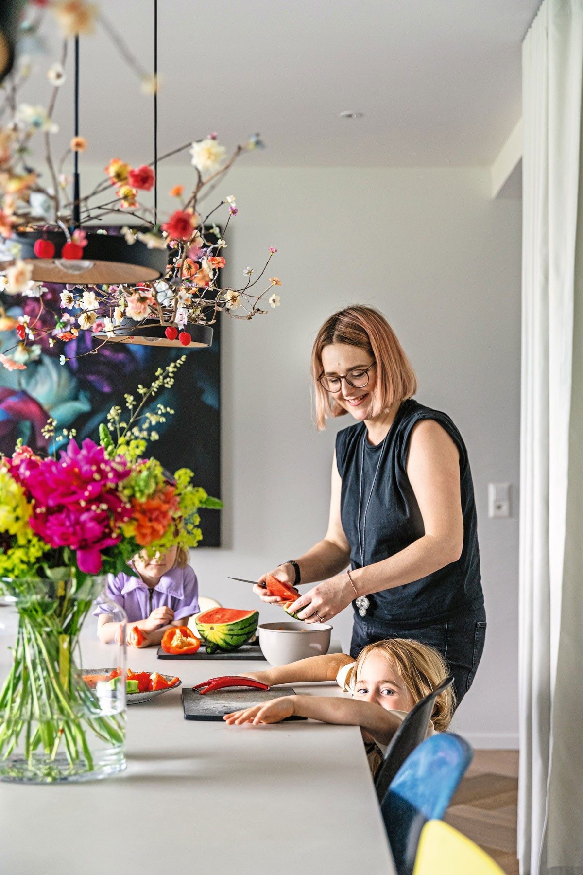 A woman and child are sitting at a table cutting up a watermelon. 