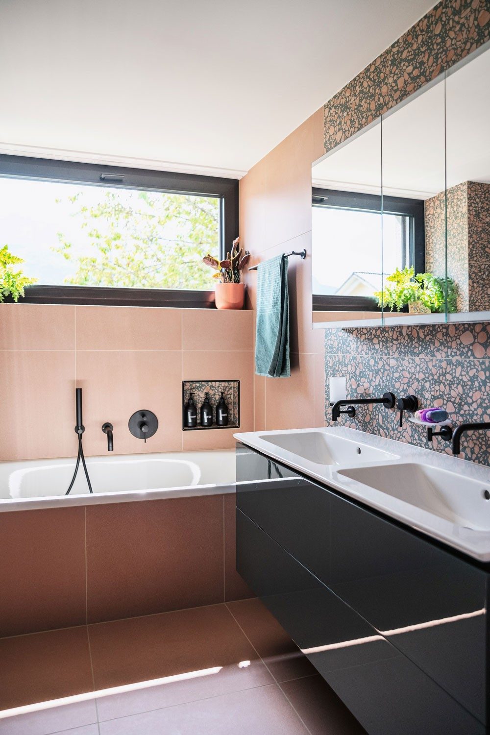A bathroom with pink tiles and a black washbasin cabinet.