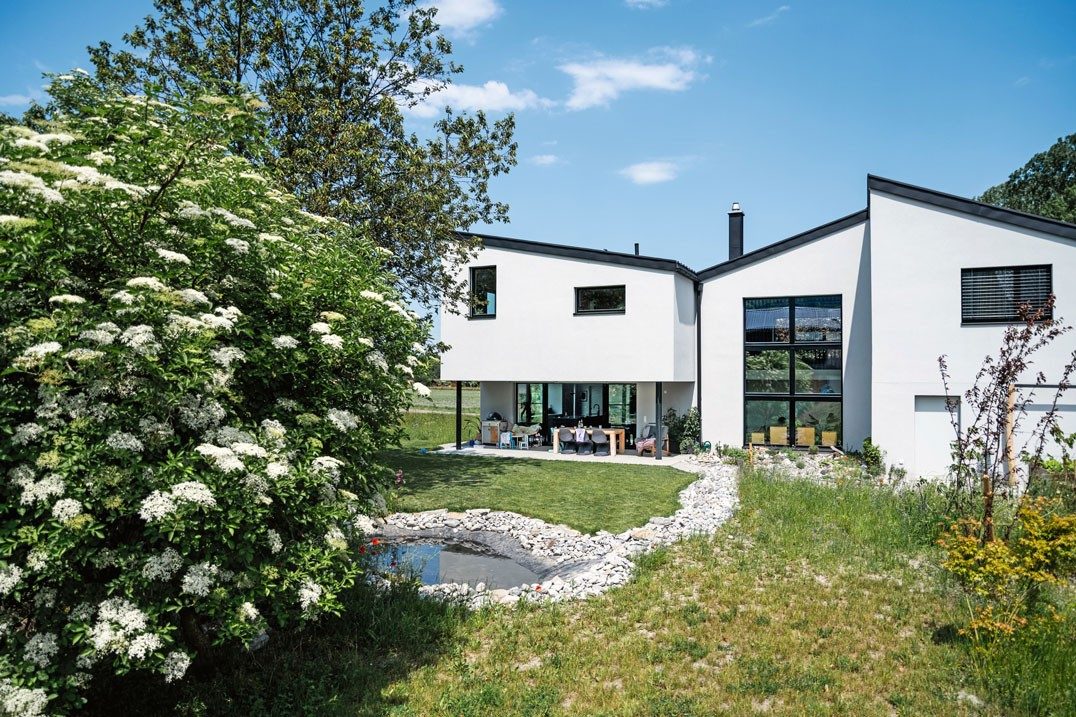 A house with three different pitched roofs, with a flowering tree and a small pond in front of it.