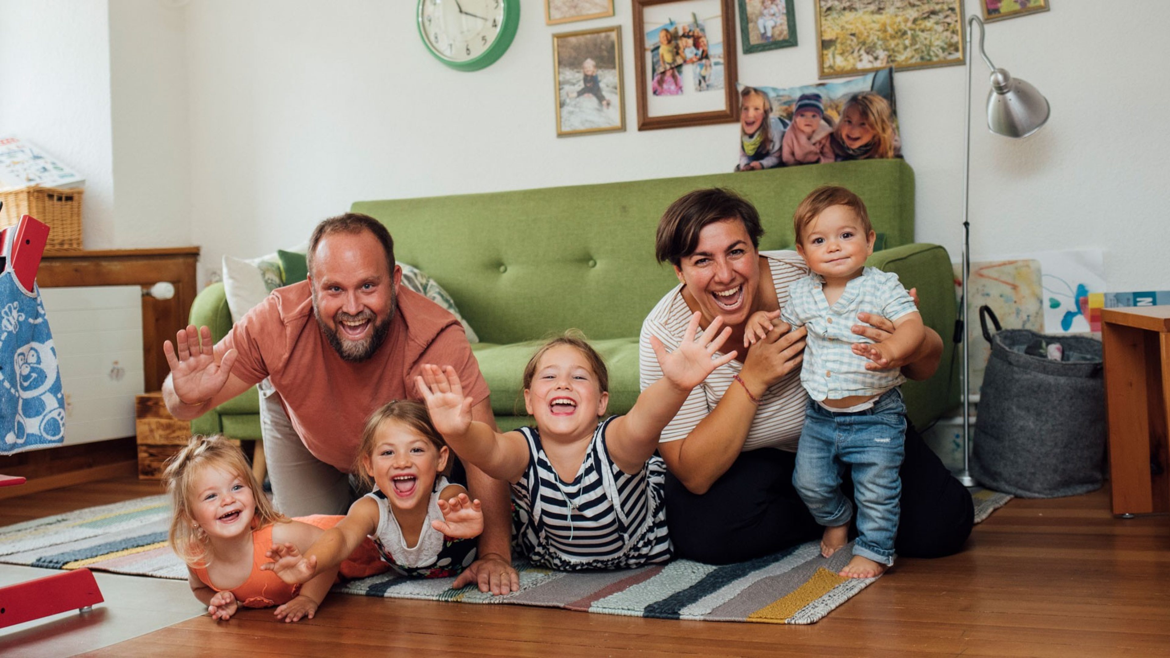 Parents with children laughing in a living room with a green sofa and pictures on the wall
