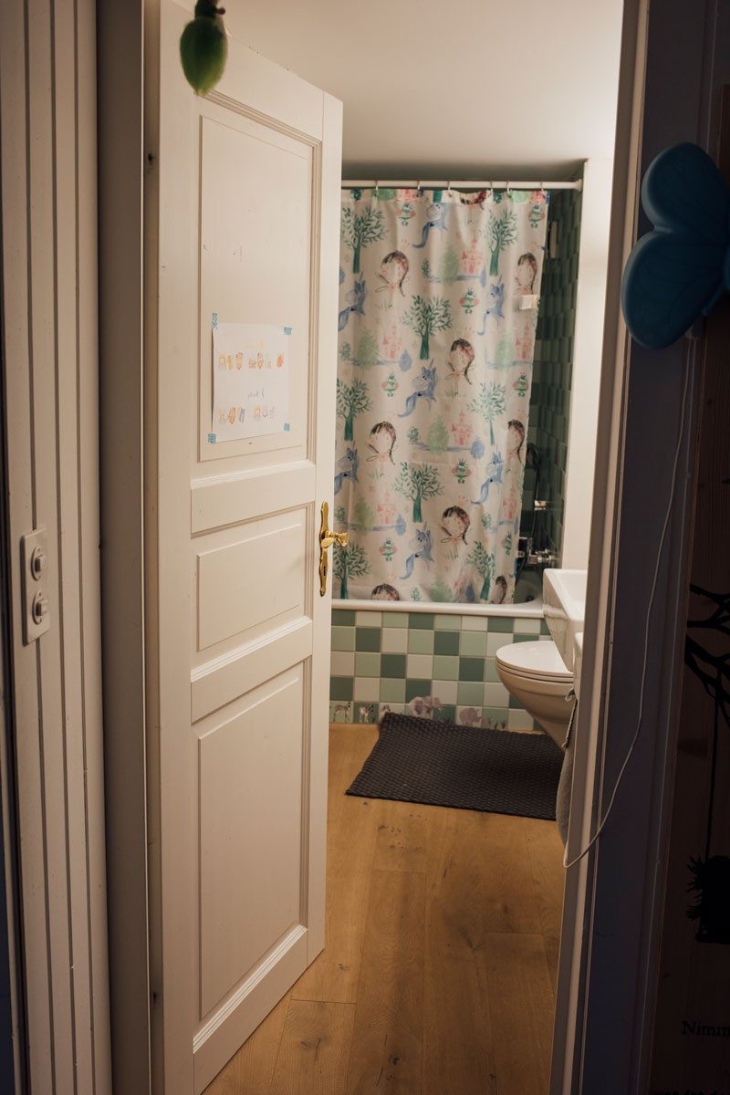 An open door to a bathroom with bathtub and shower curtain.