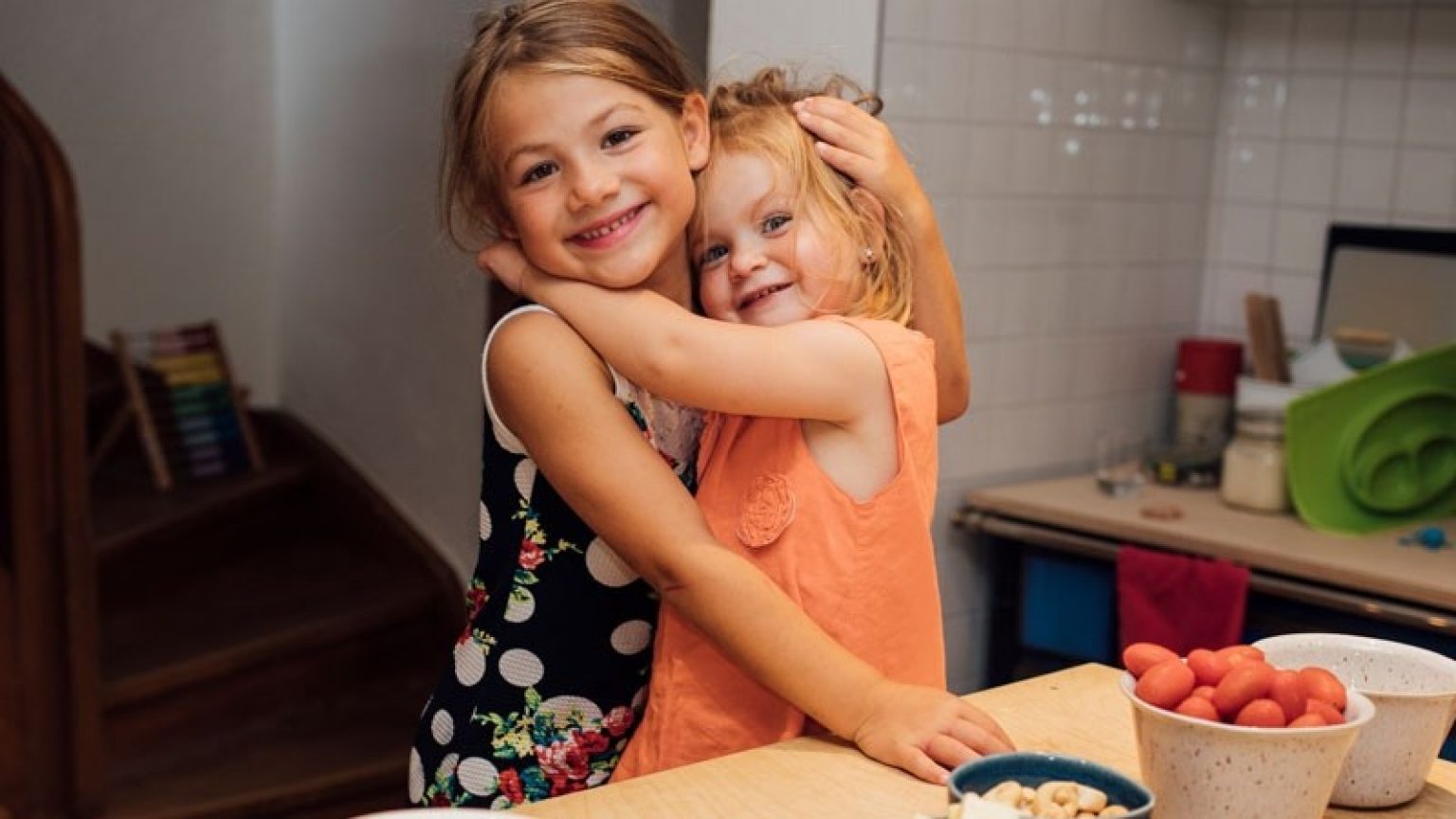 Two girls stand in a kitchen hugging each other.