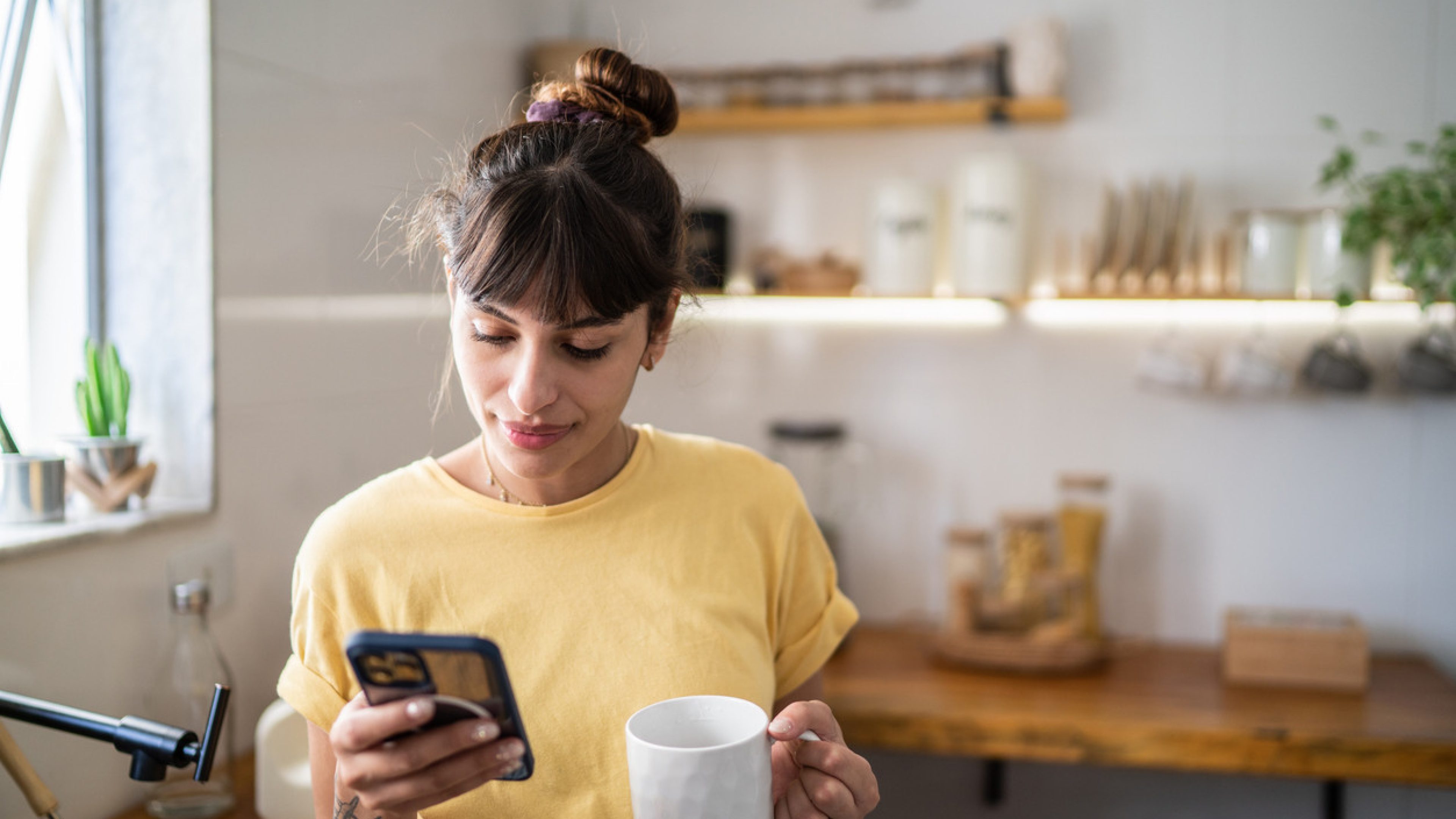 Young woman using the mobile phone while drinking coffee or tea at home