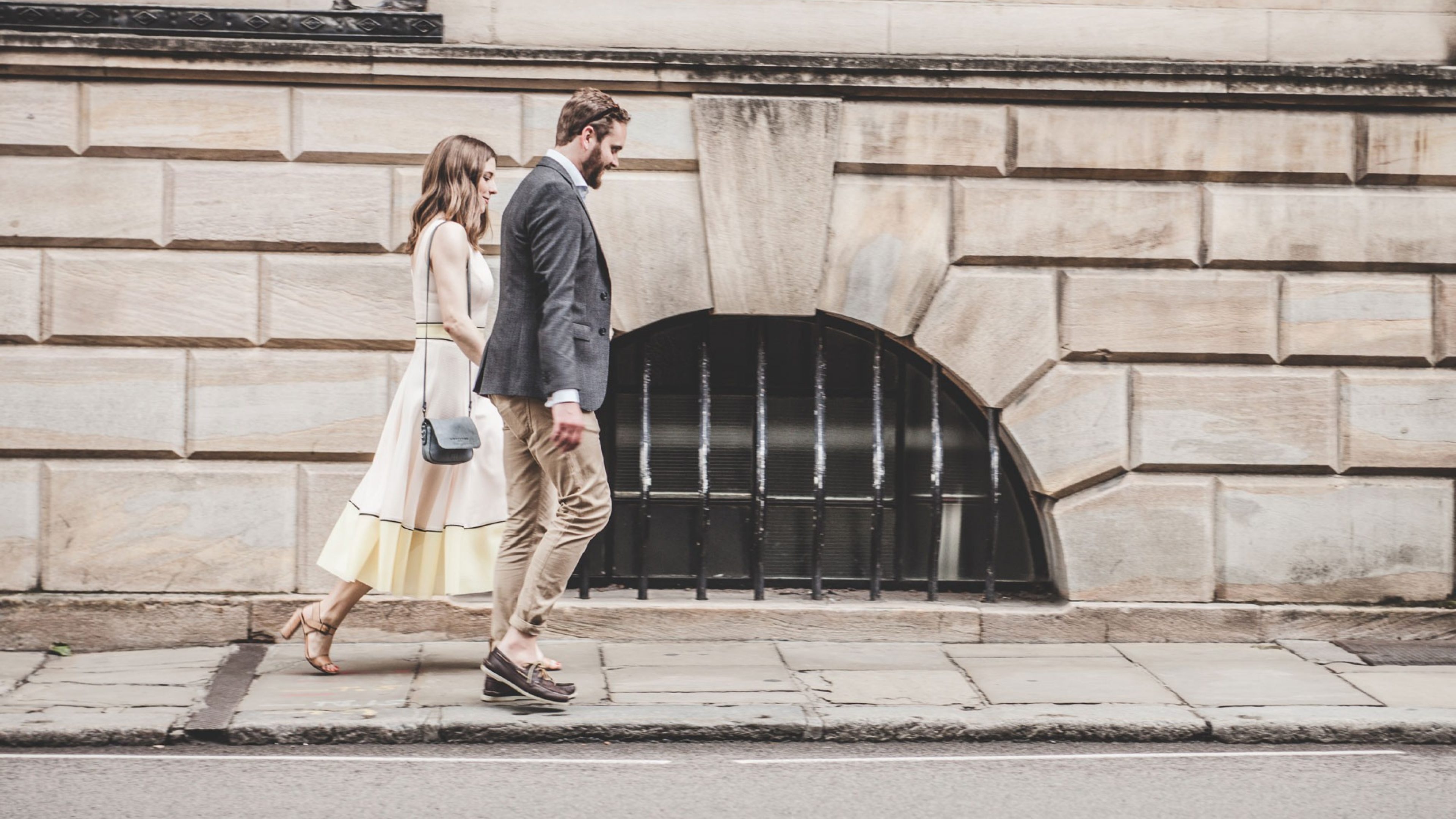 A couple walking hand-in-hand on the pavement in front of a building
