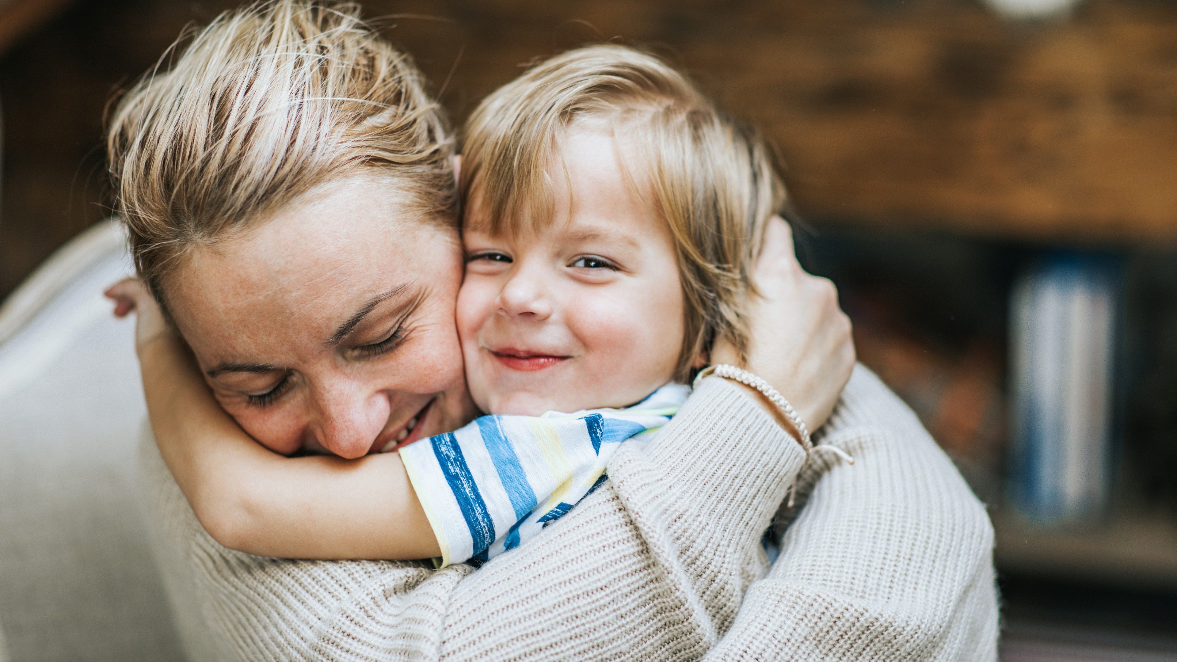 Happy mother embracing her small son at home, while boy is looking at camera.