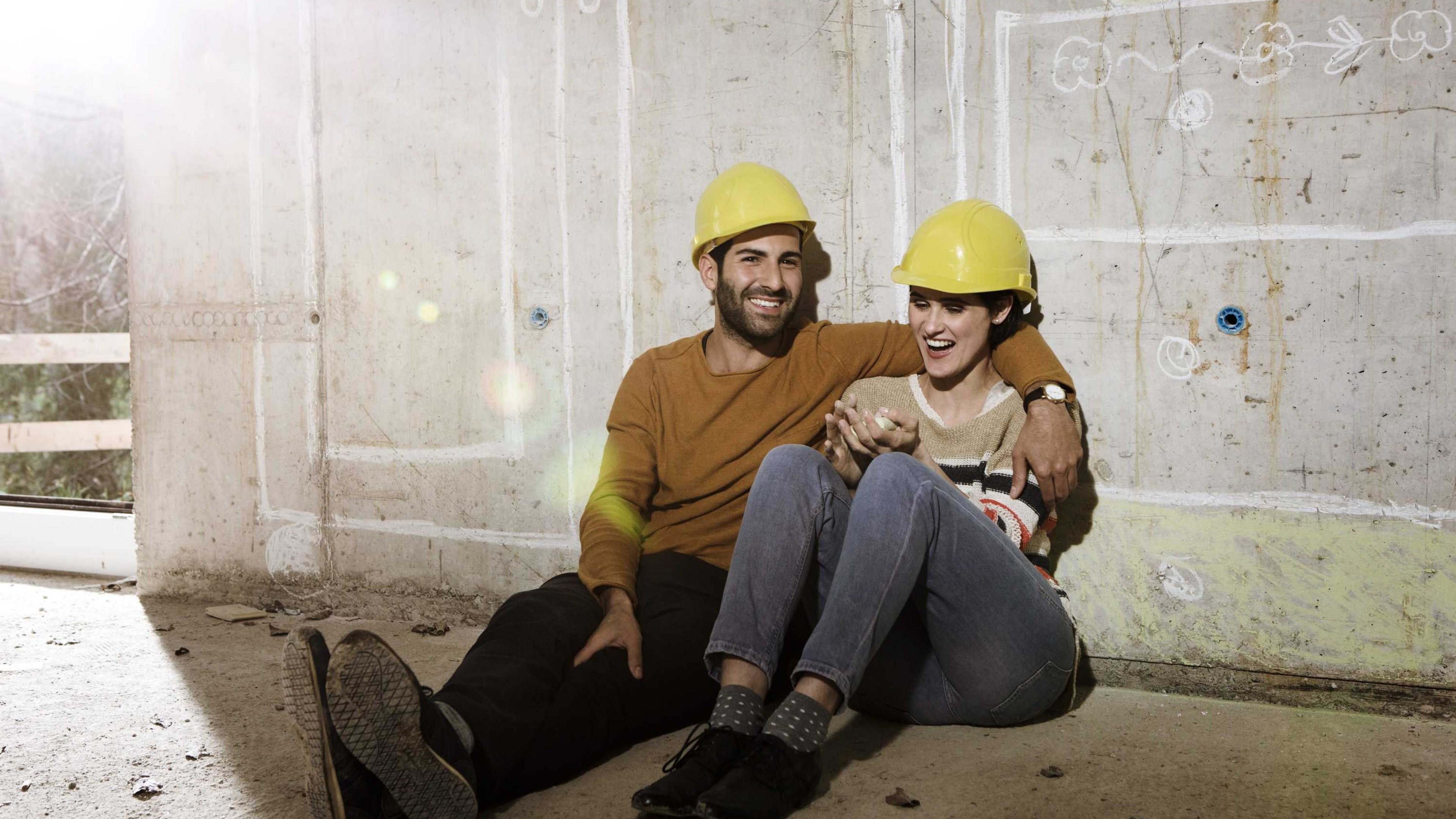 A man and woman wearing safety helmets sitting in front of their future home