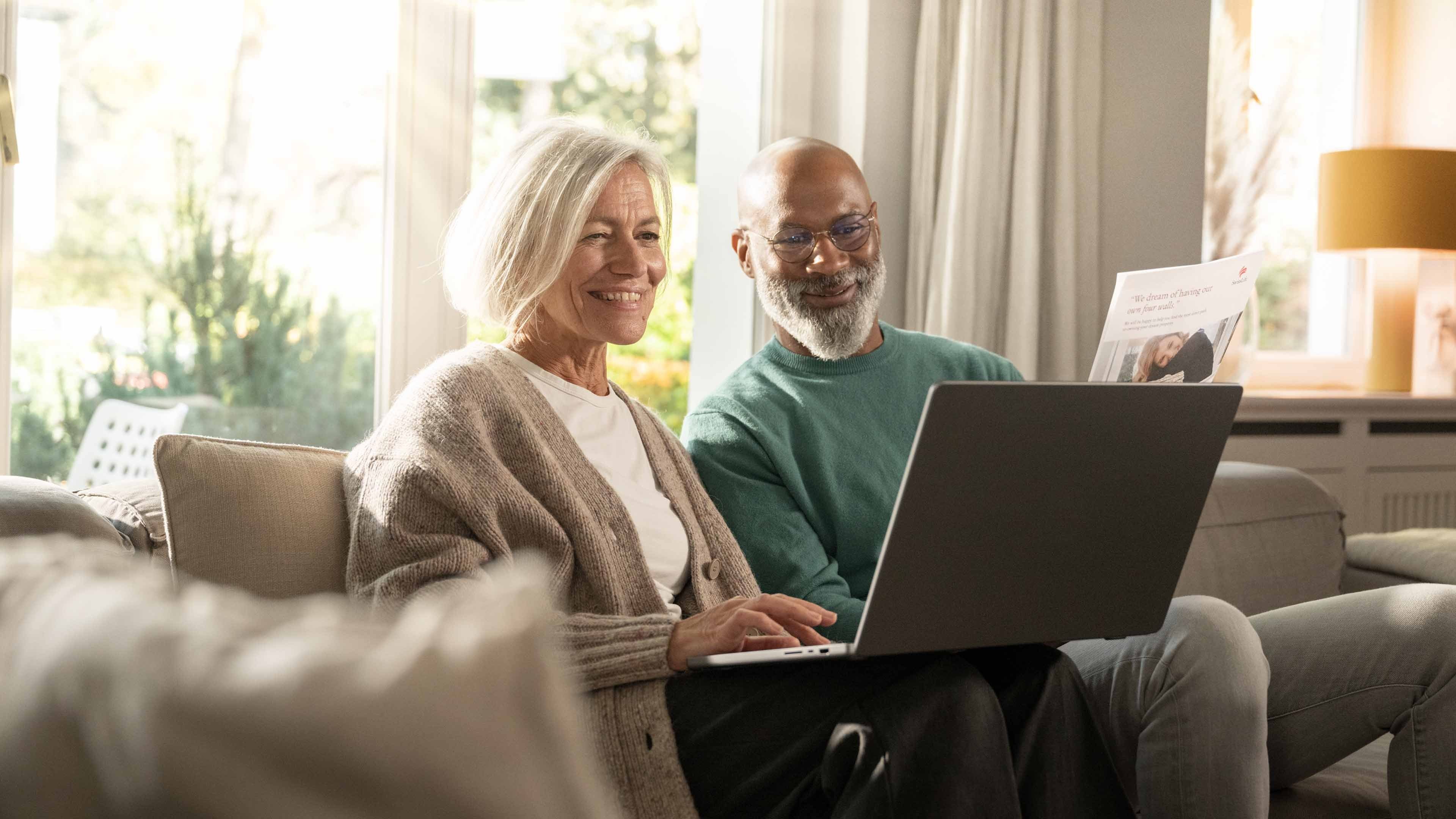 An older woman and an older man sitting on the sofa with a laptop during a digital consultation