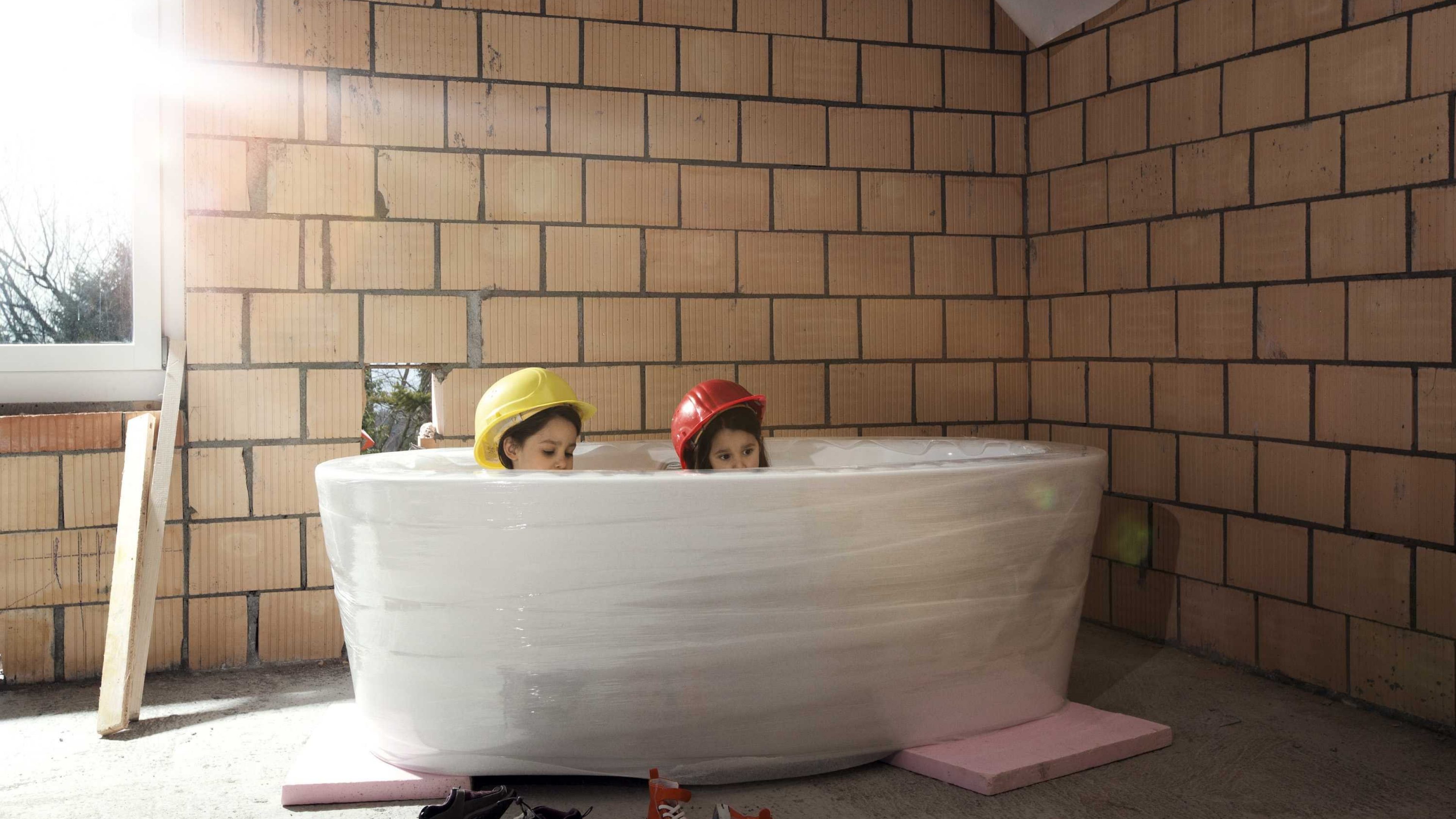 Kinder sitzen in einer Badewanne im Rohbau eines Hauses.