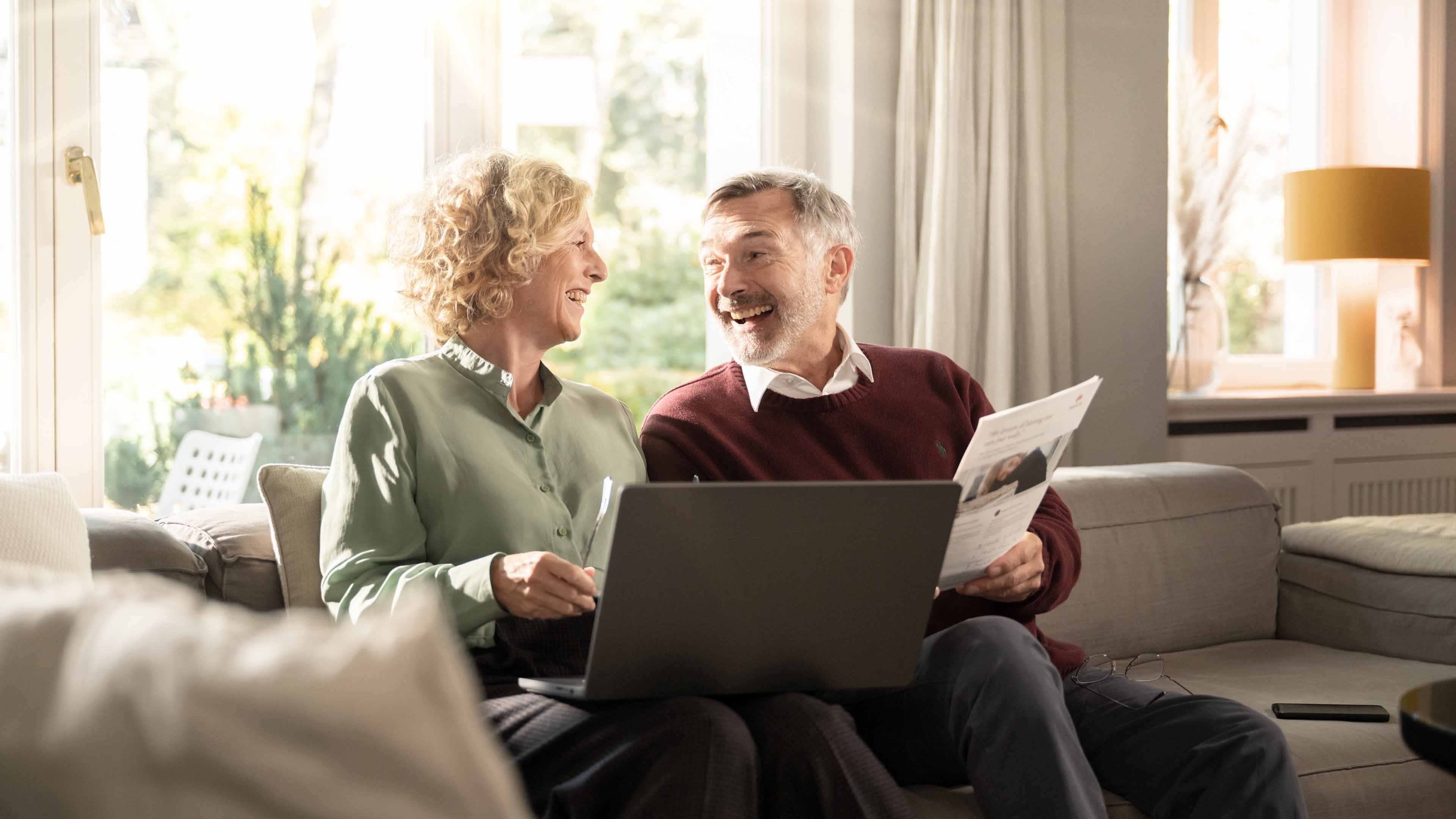 A man and woman sitting on a sofa holding a Swiss Life brochure