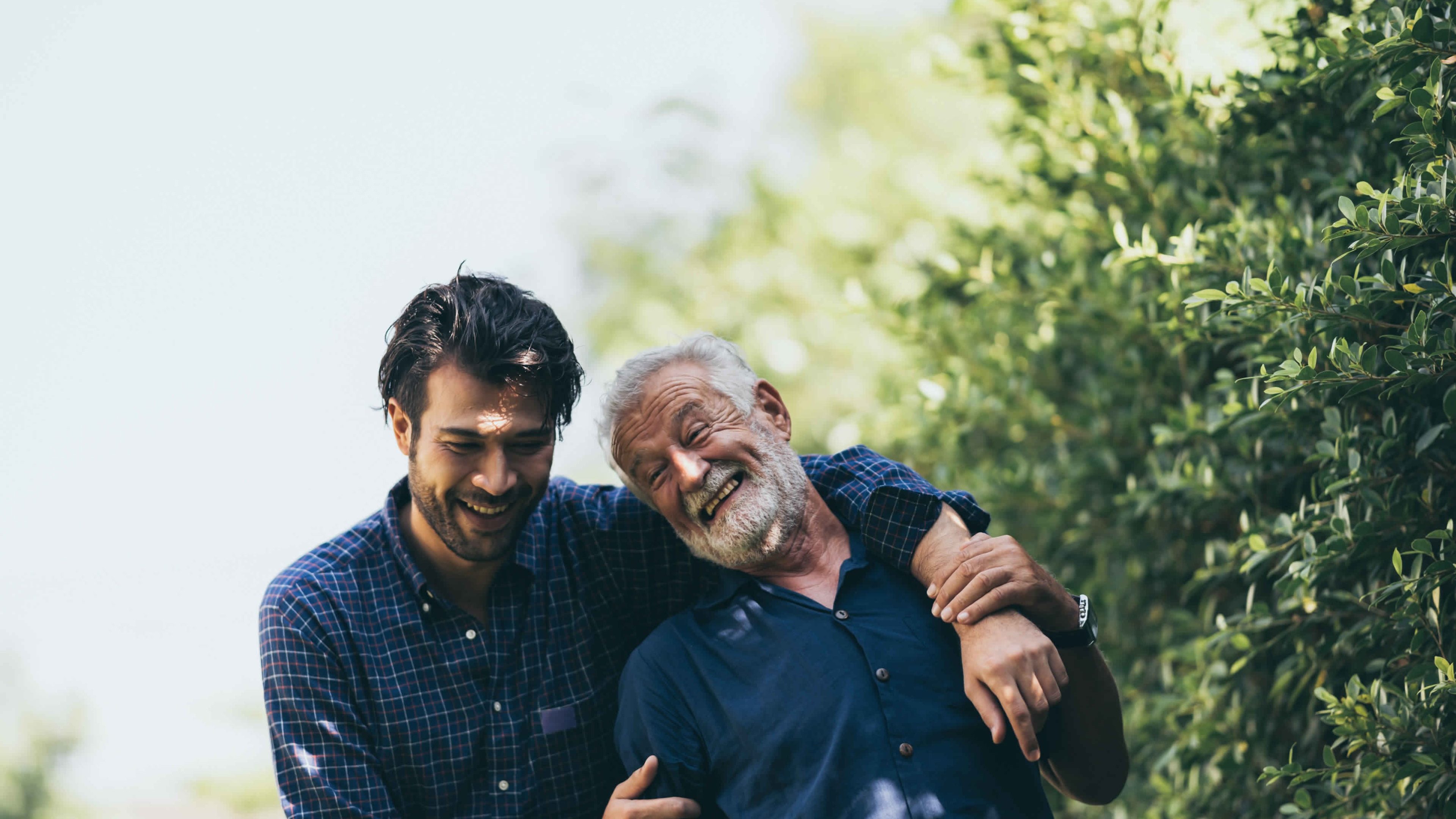 Father and son stand in front of trees and hug each other laughing