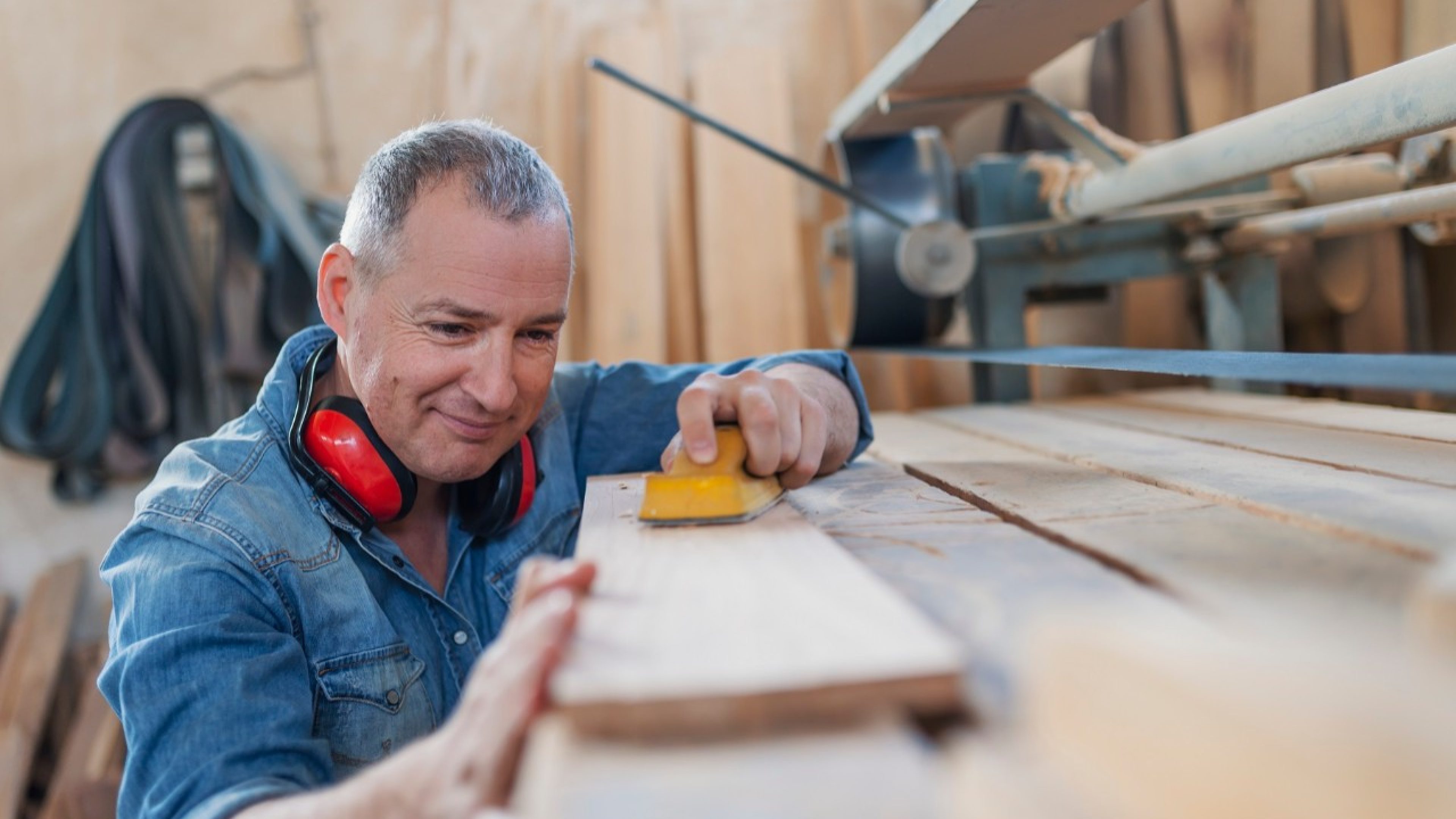 Image of male joinery worker smoothening piece of wood. Hardworking carpenter polishing wood using abrasive paper. Carpentry workshop routine.
