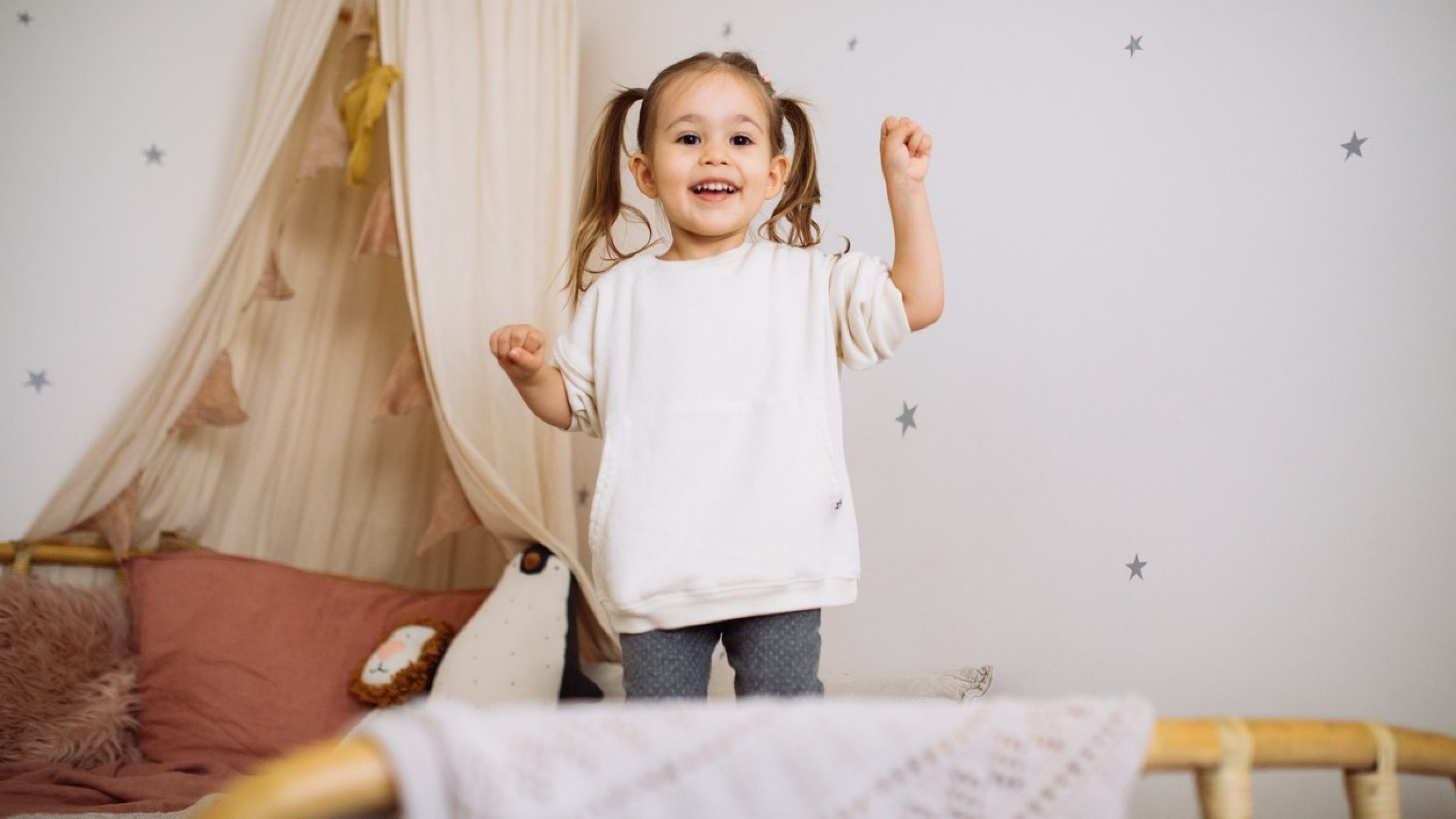 Happy child girl jumps and plays bed