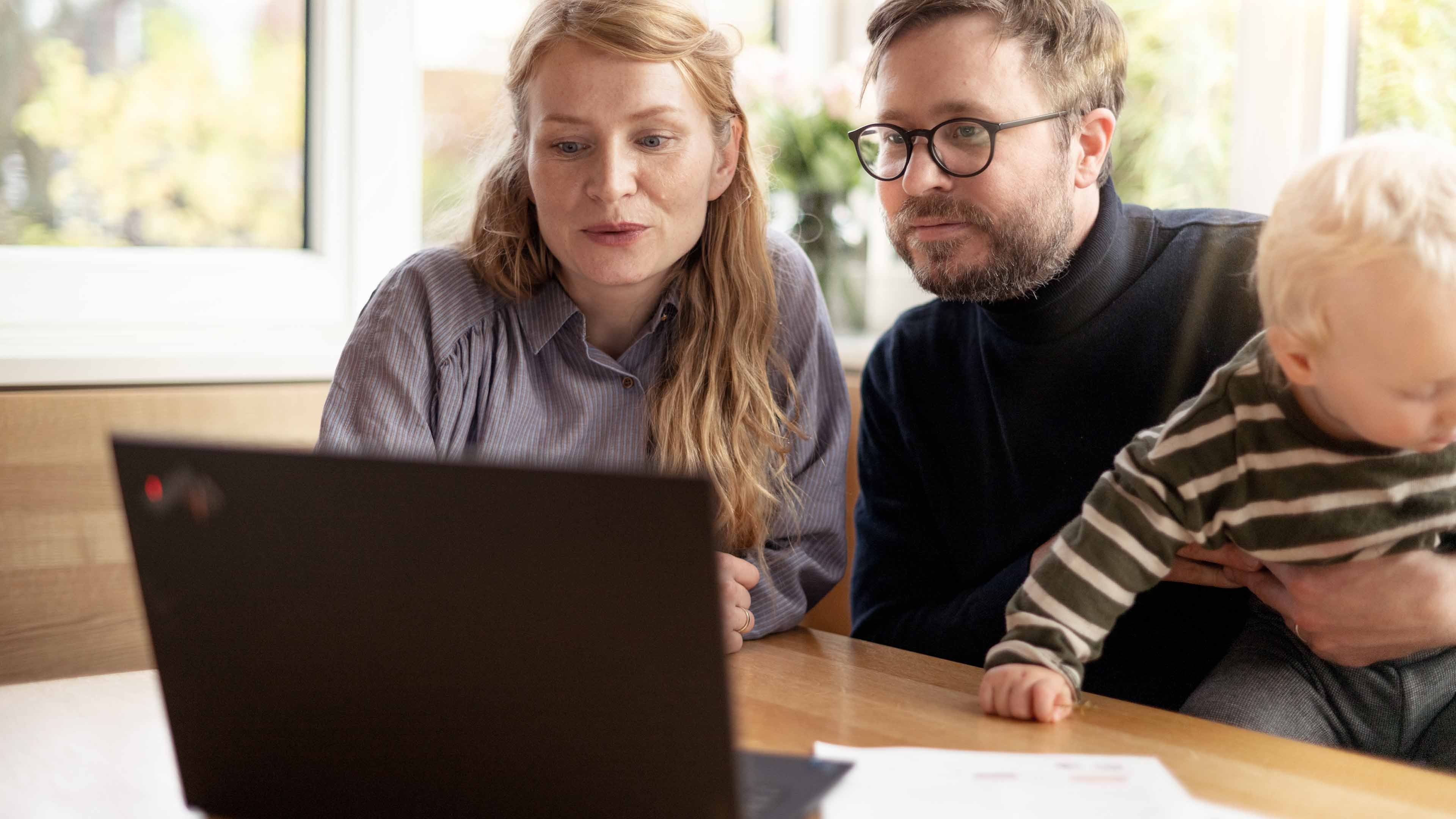 A father holding a small boy and a mother in front of a laptop