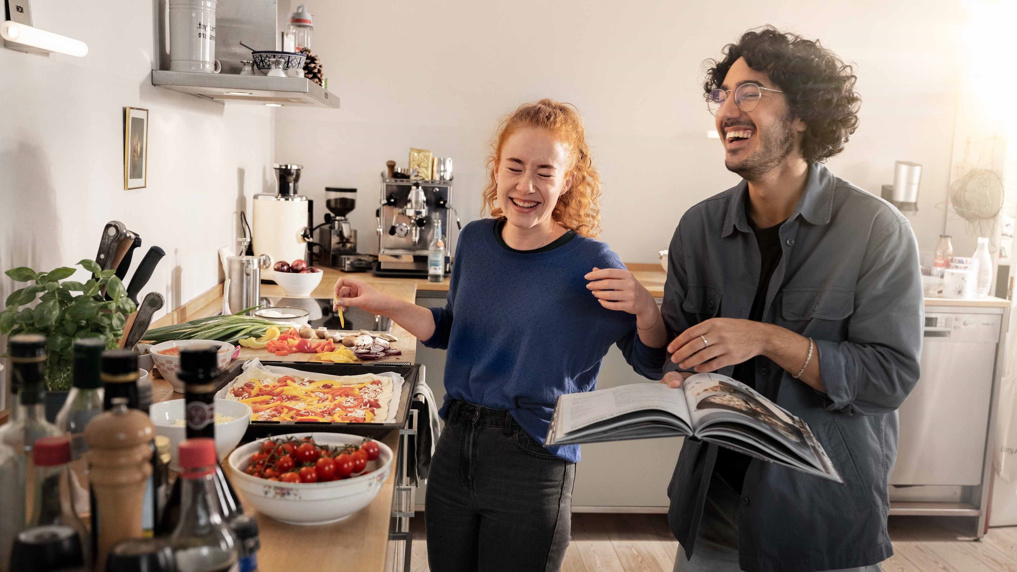 A young man and woman topping a pizza base