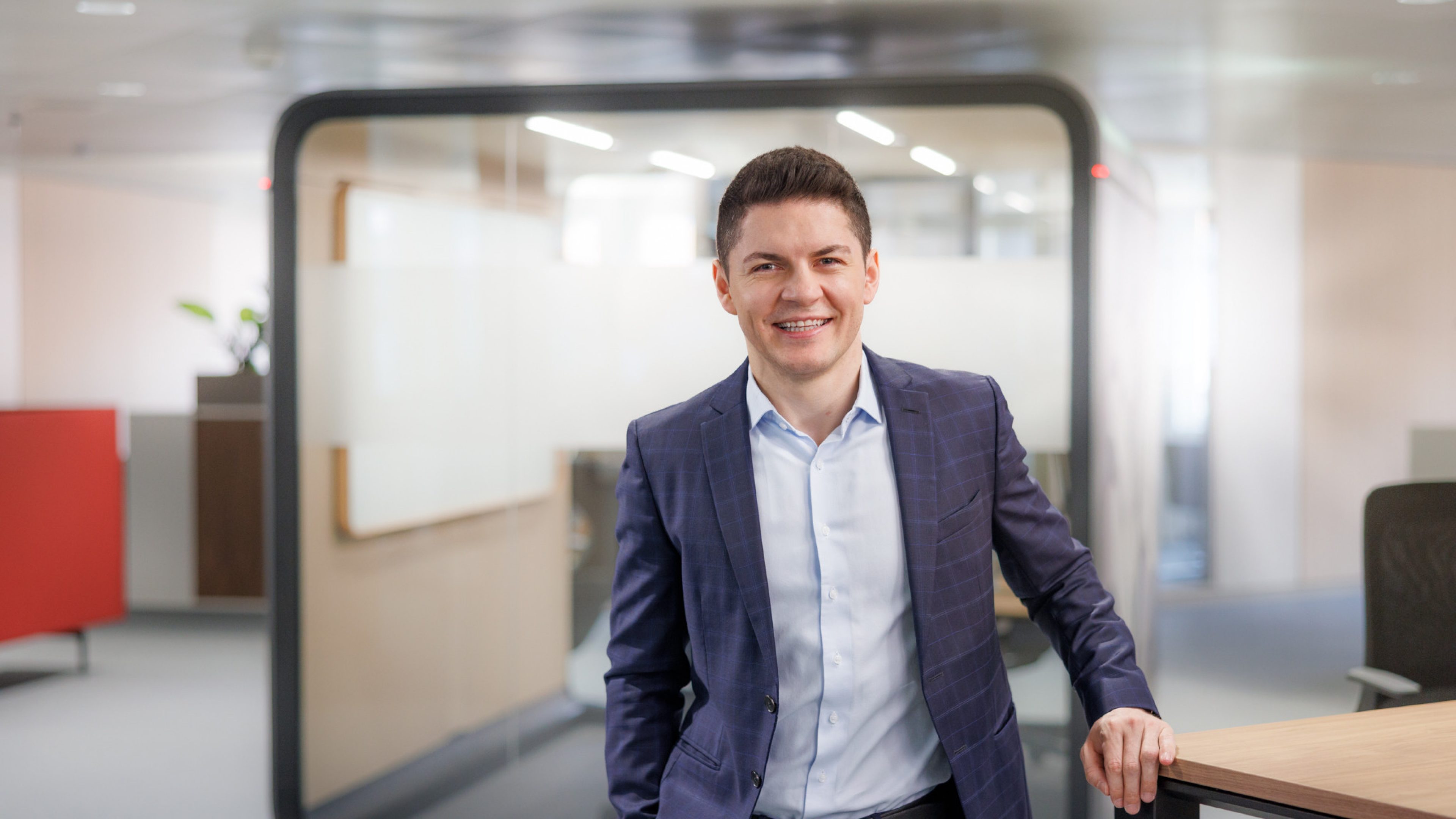 Male Swiss Life employee in a modern office, smiling at the camera.