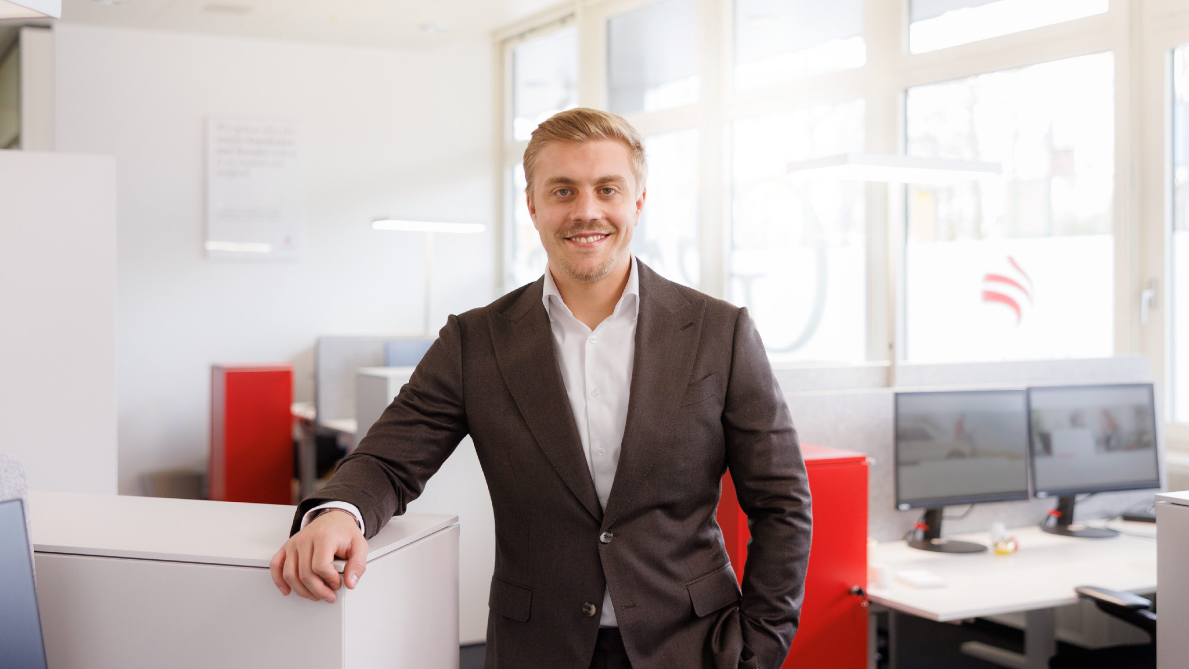 Male Swiss Life employee in a modern office, smiling at the camera.