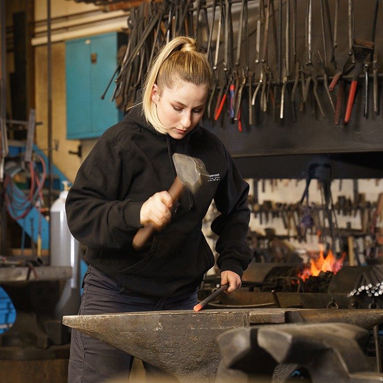 Woman standing and working in a forge.