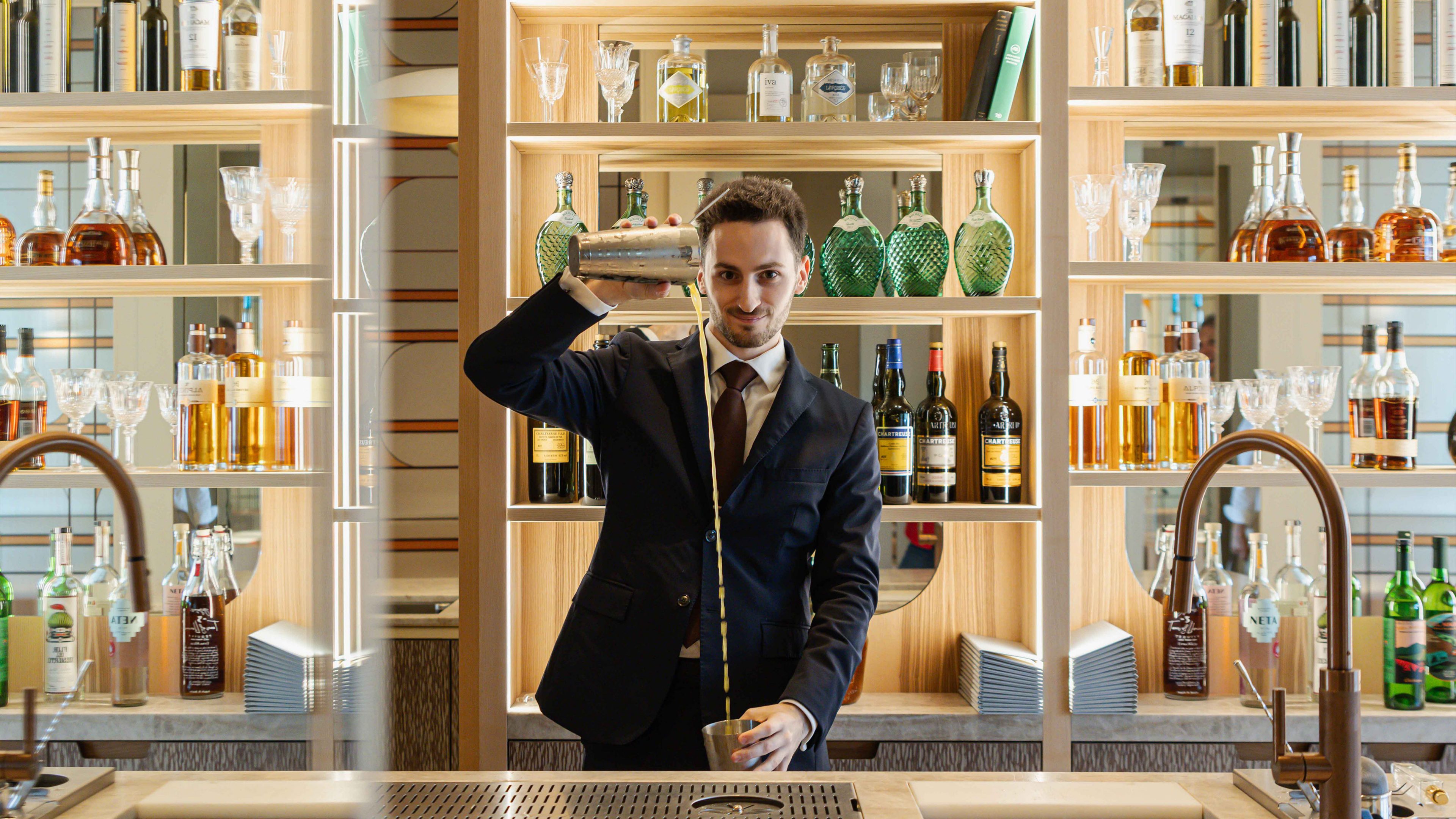 Le mixologue Alexandre Besnault verse une boisson et se tient derrière le bar en marbre du Restaurant Pic.