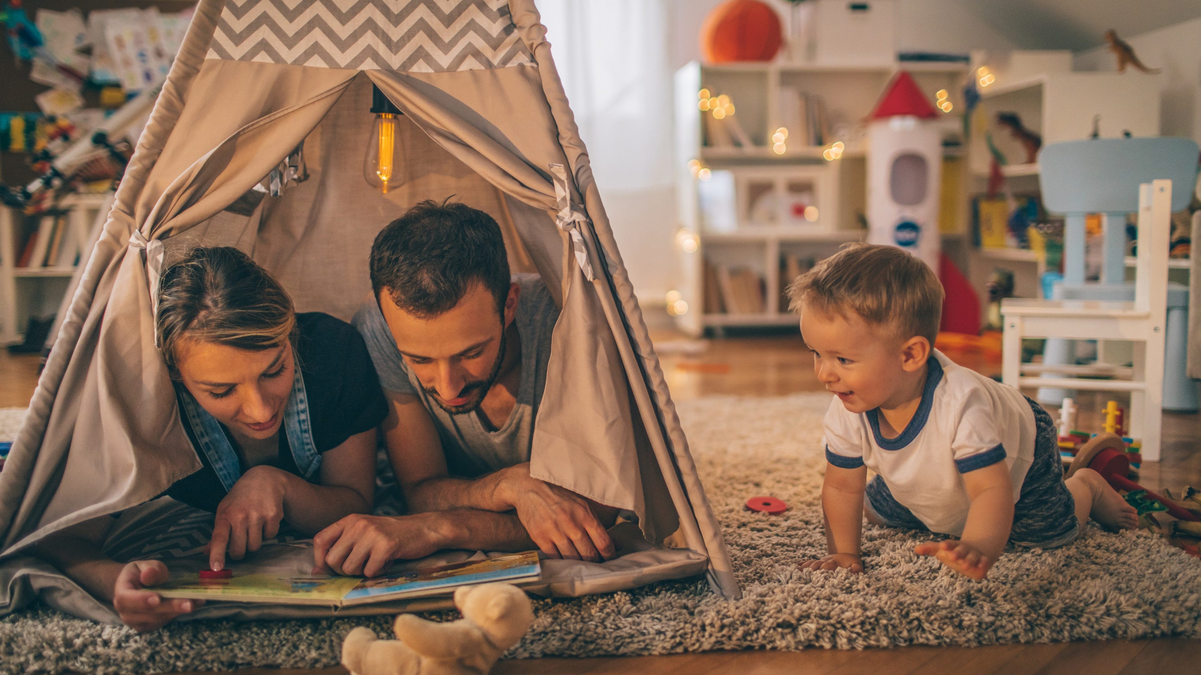 Photo of a young family with one child, spending time together indoors, playing 'Indians and cowboys' in their boy's wigwam