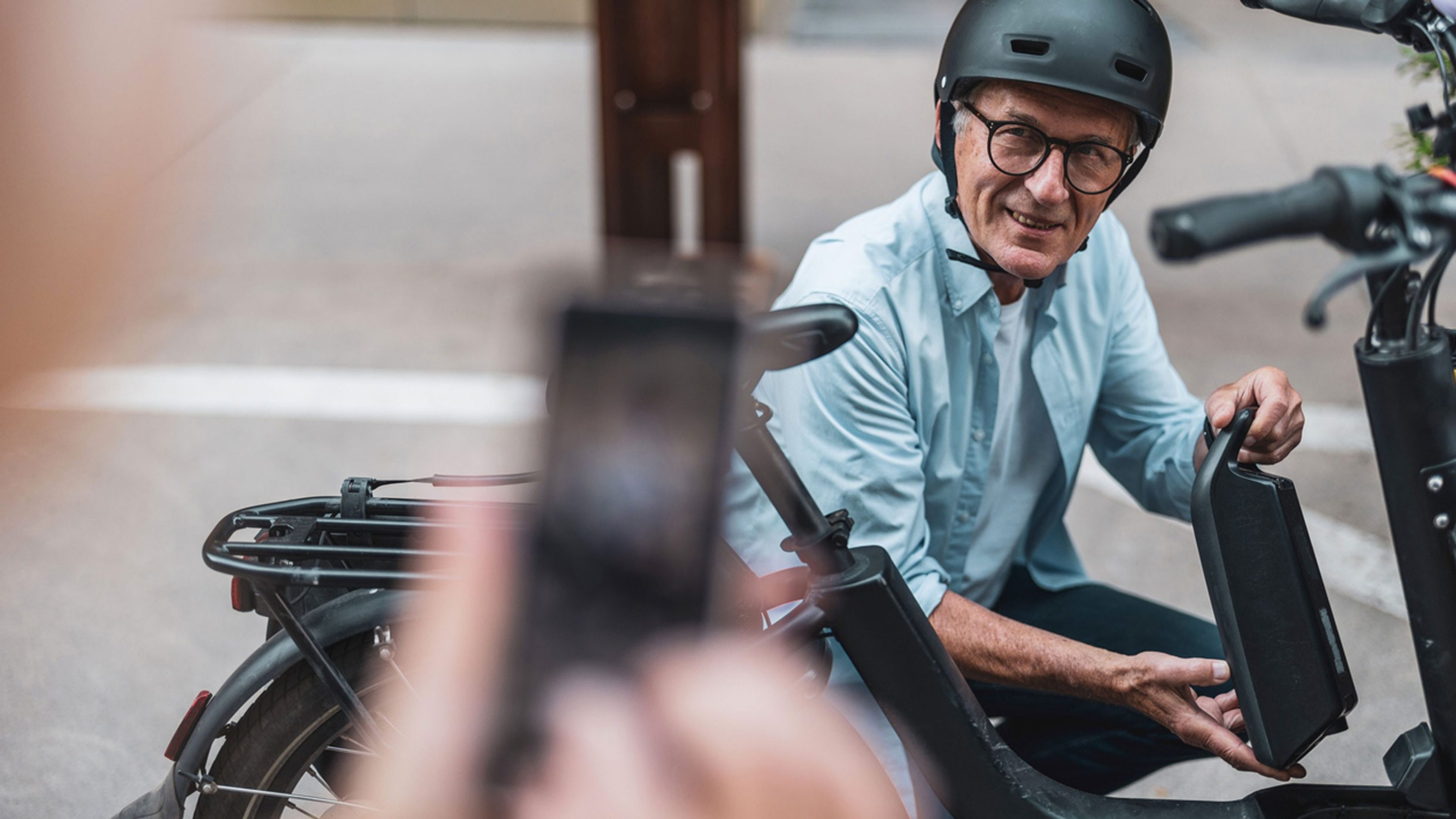 Un homme s’agenouille près de son vélo électrique et tient sa batterie dans les mains.