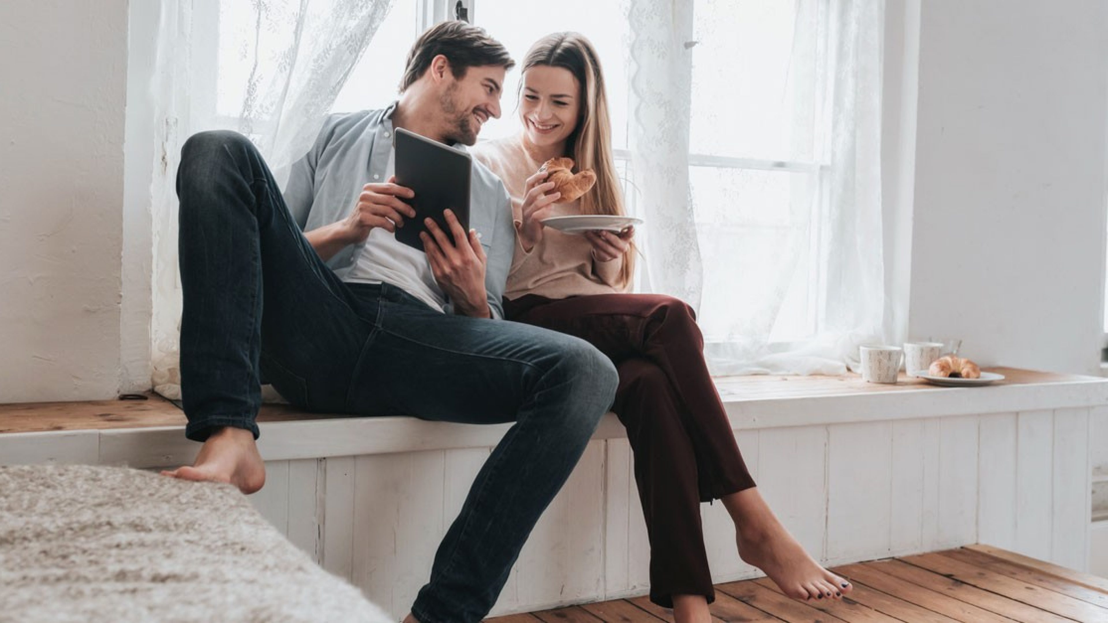 Jeune couple dans son logement en propriété qui regarde quelque chose ensemble sur une tablette.