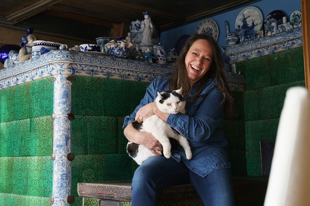 Une femme avec un chat sur les genoux rit devant la caméra.