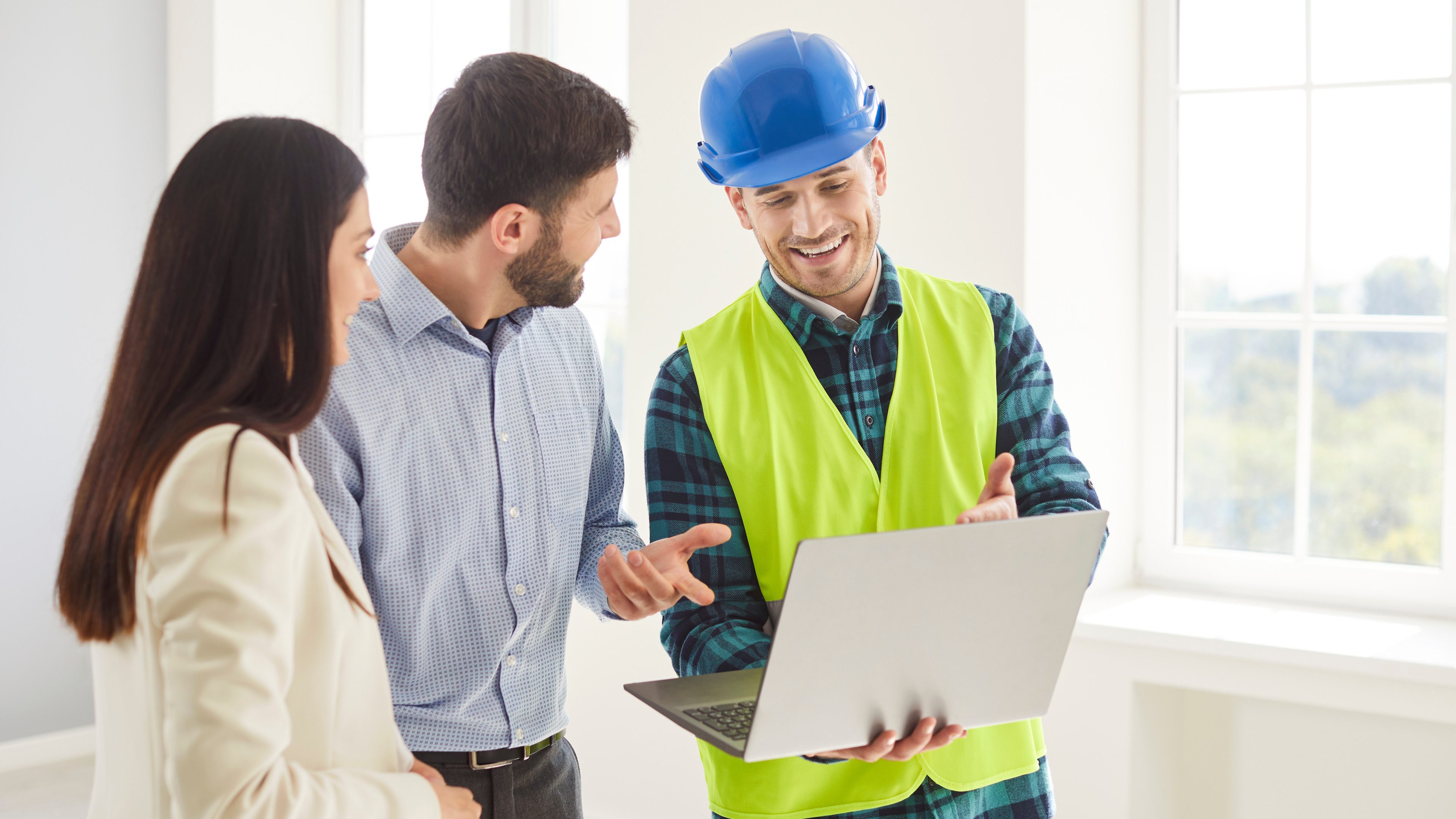 Un chef de chantier et un couple regardent dans leur maison nouvellement construite sur leur ordinateur portable