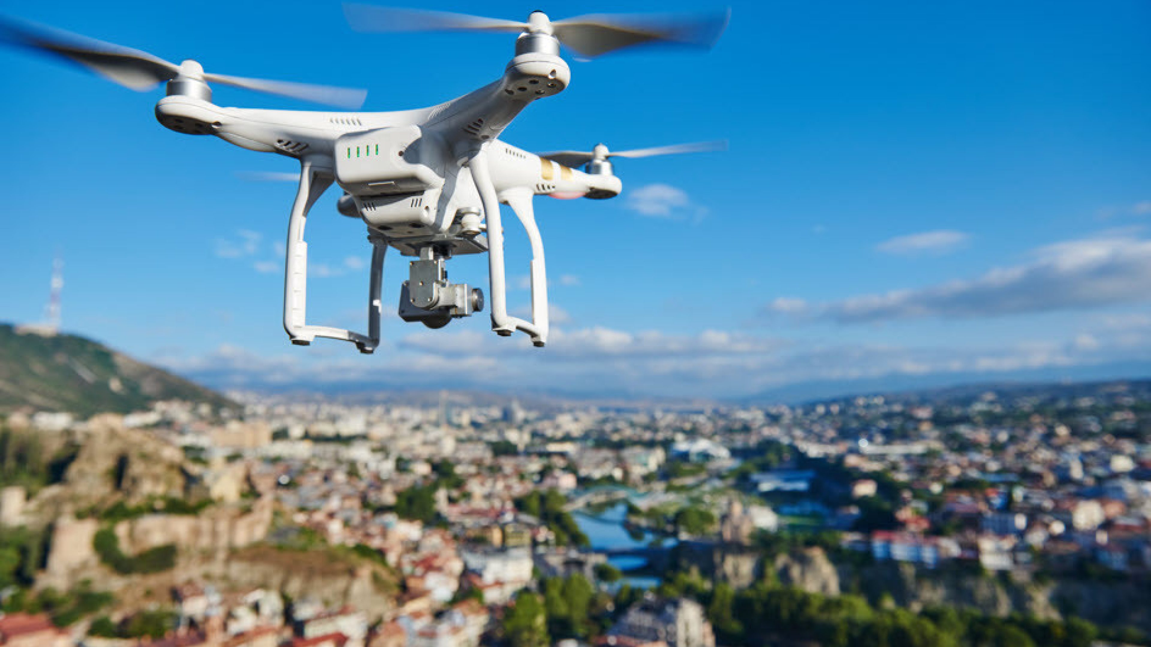 Un drone blanc vole dans le ciel au-dessus d’une ville.