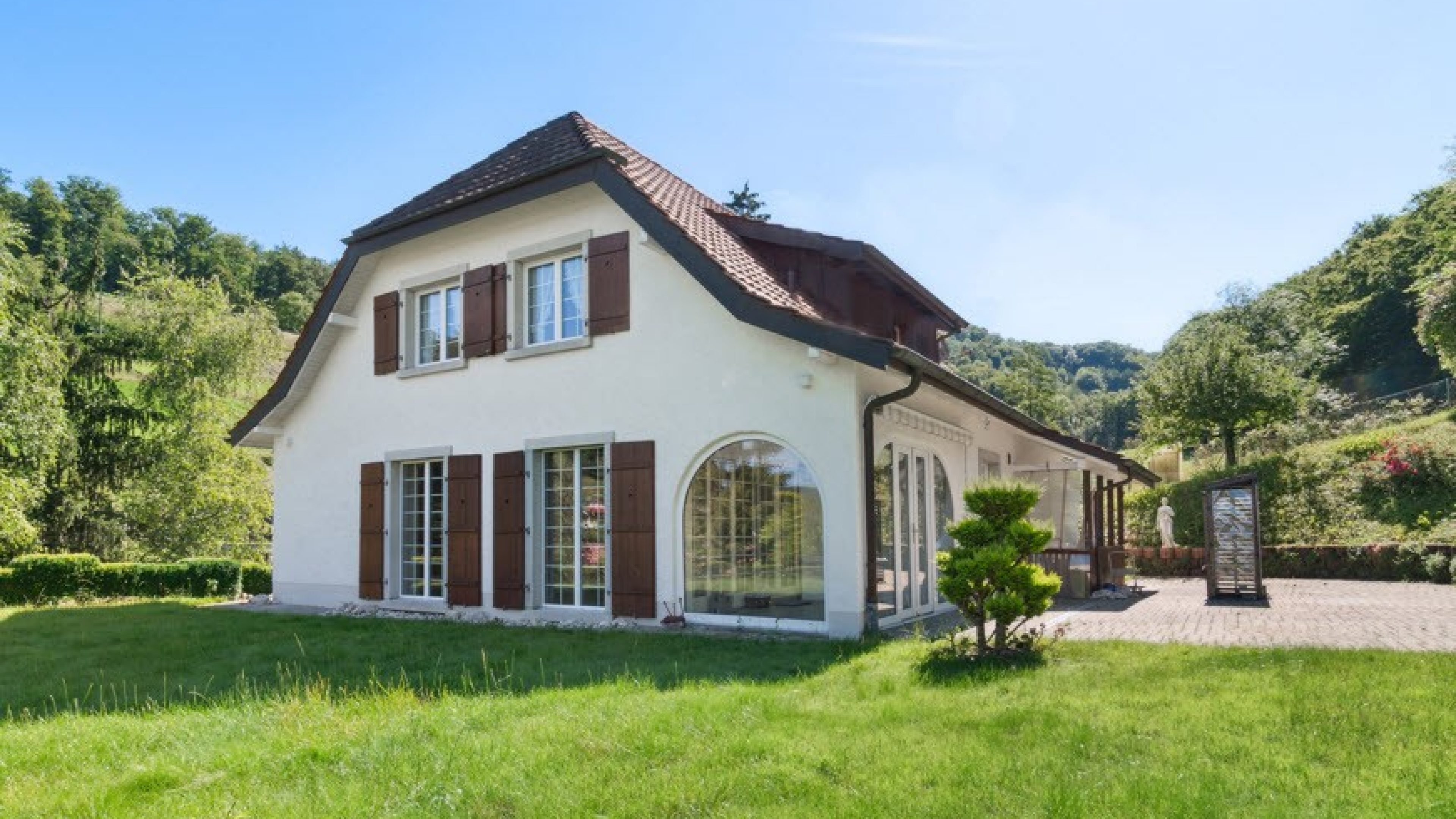 Maison individuelle aux volets bruns, entourée d’une nature verdoyante