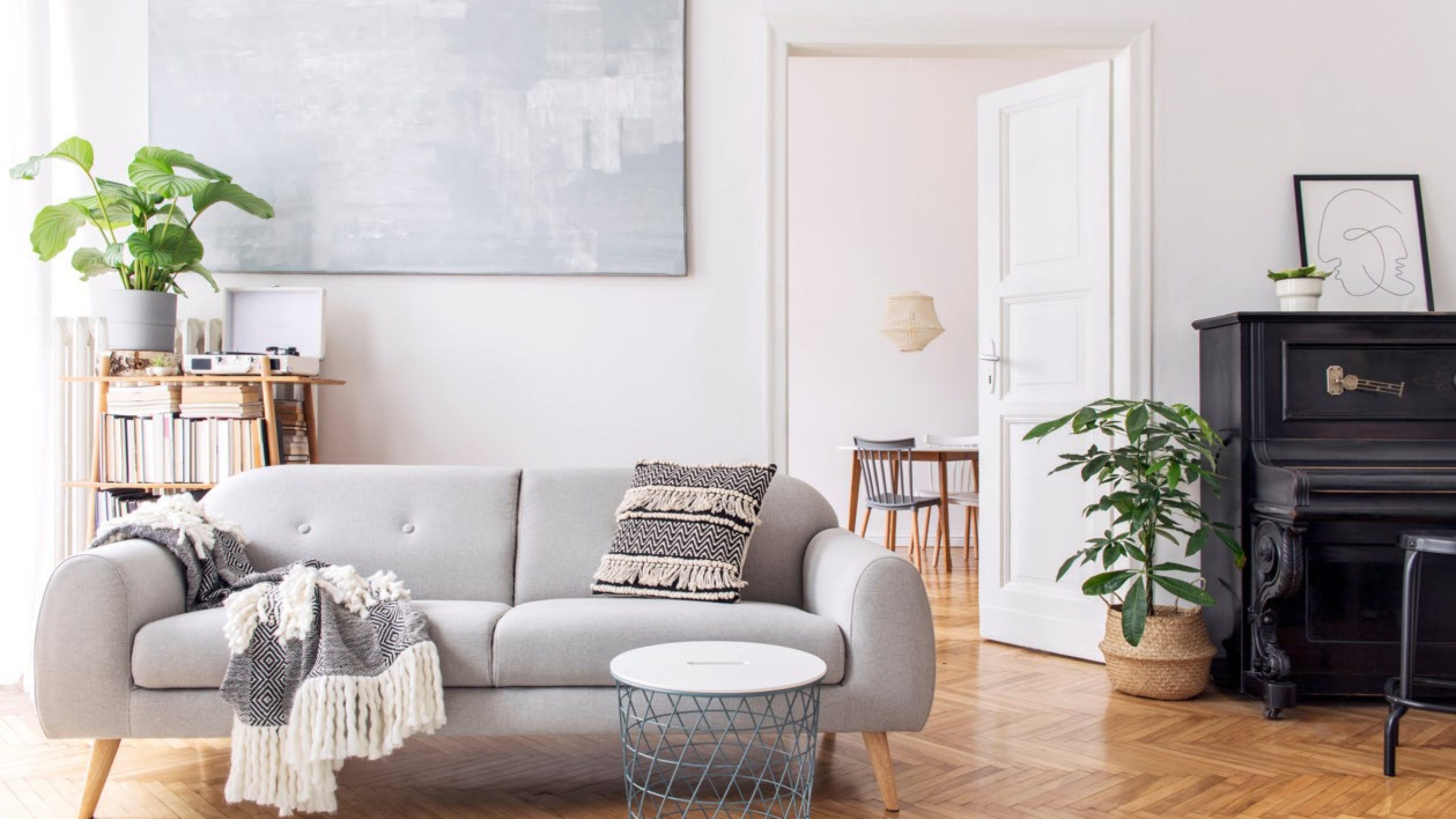 Un salon lumineux avec parquet accueille un canapé gris clair et un piano noir.