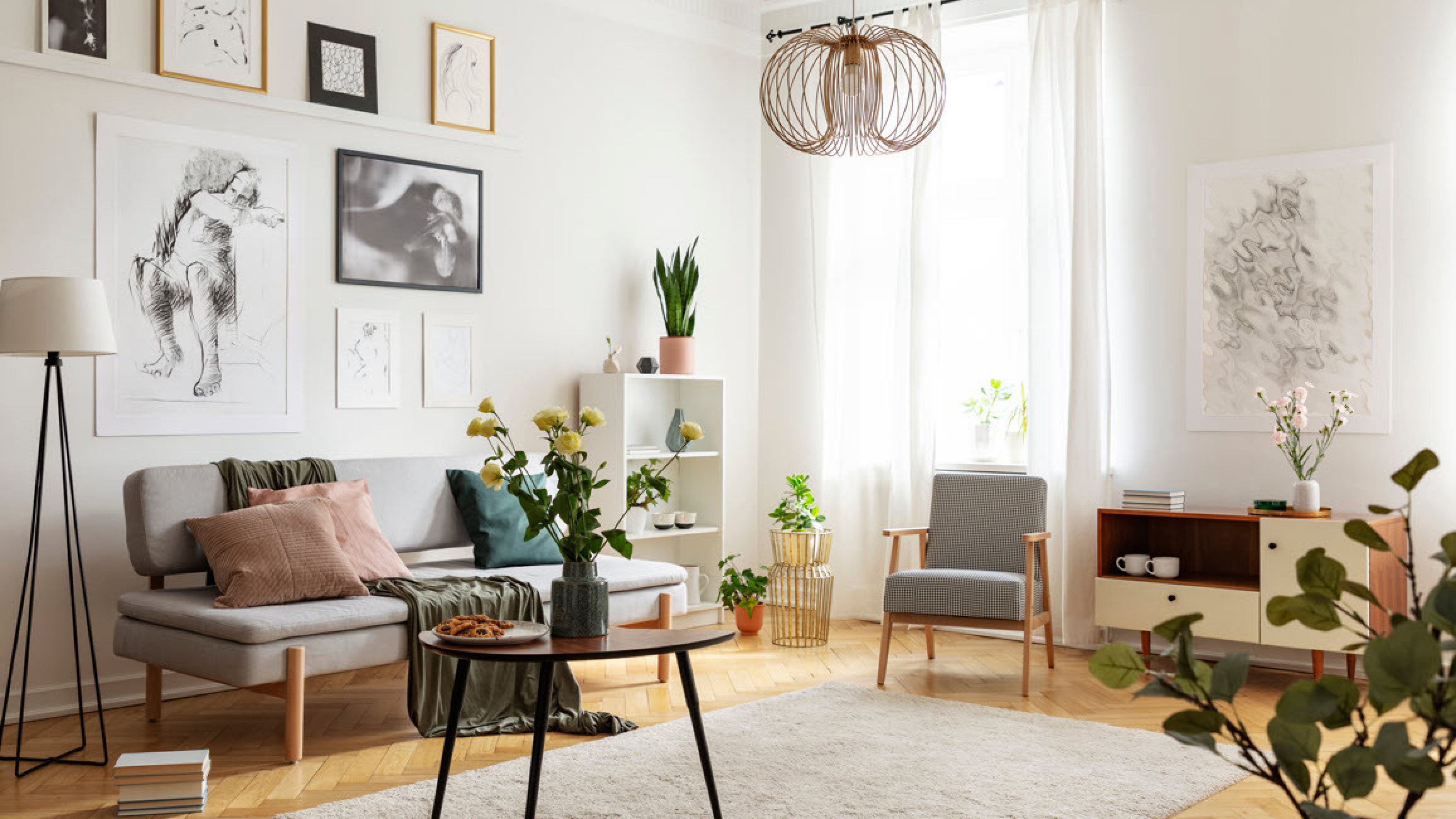 Salon lumineux avec parquet, canapé, fauteuil, table de salon, fleurs et différents tableaux. 