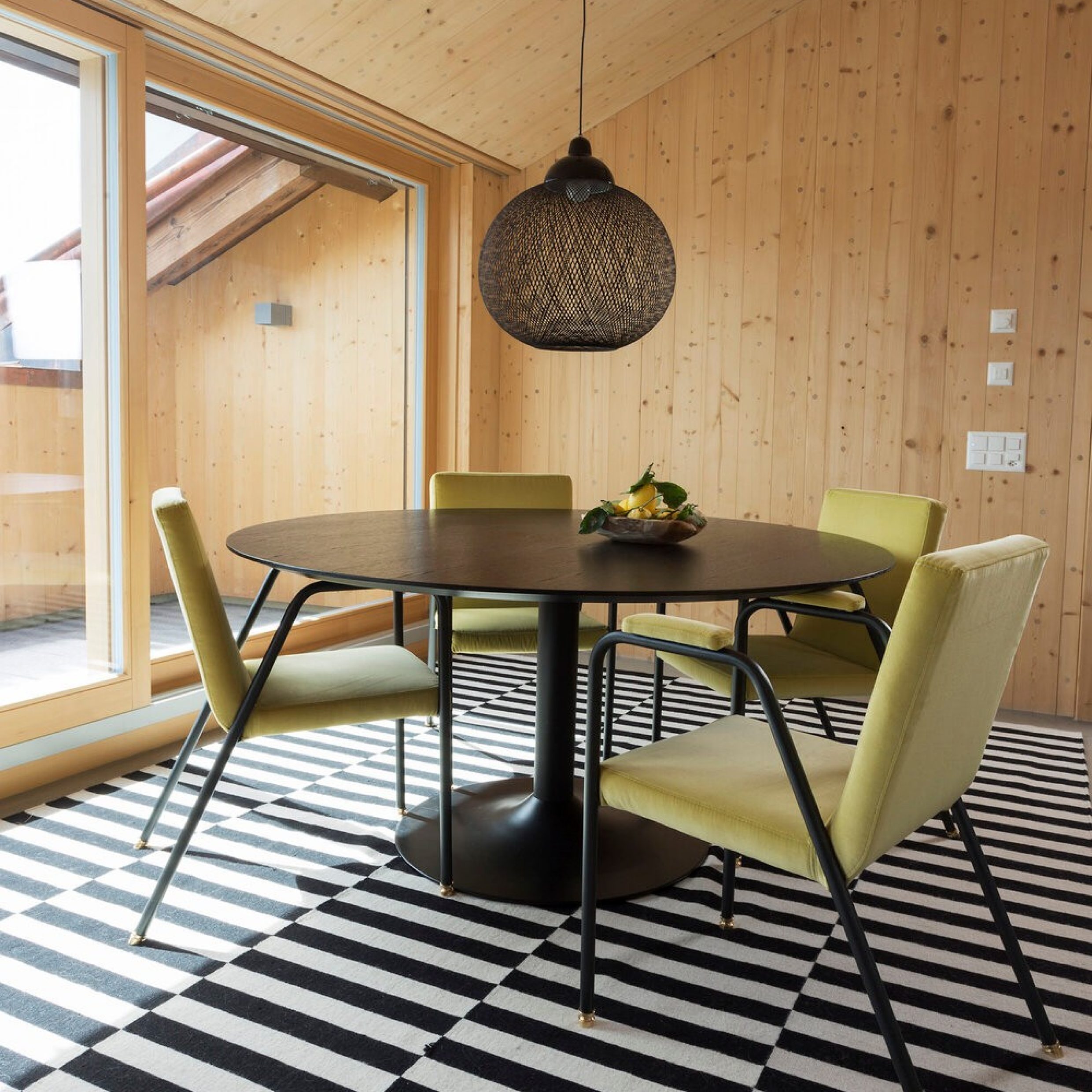 Une salle à manger avec une table ronde et quatre chaises posées sur un tapis rayé en noir et blanc.
