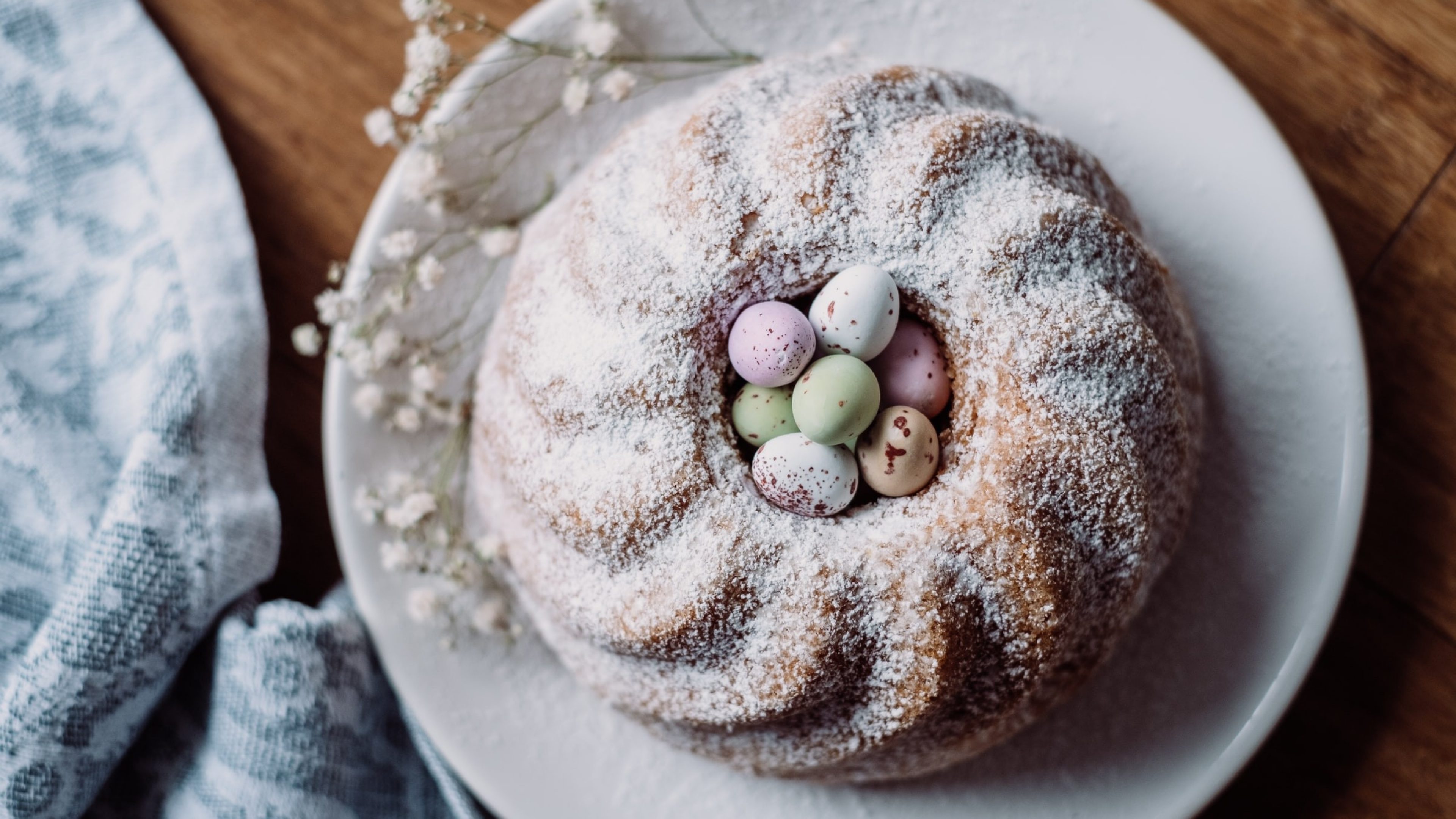 Un gâteau rond saupoudré de sucre glace, au centre duquel sont déposés de petits œufs de Pâques.