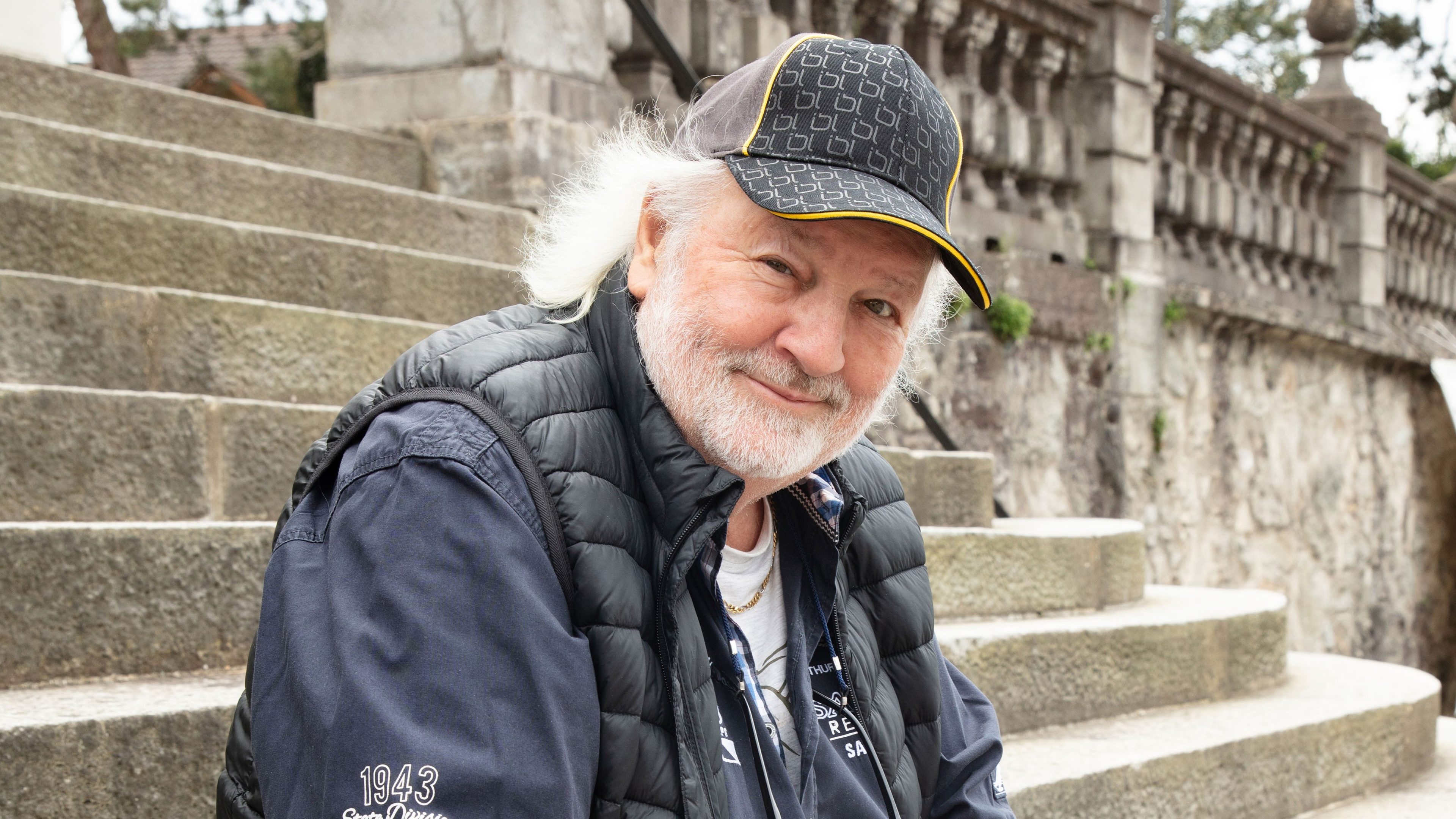 Un homme plus âgé et souriant est assis dans un escalier dehors