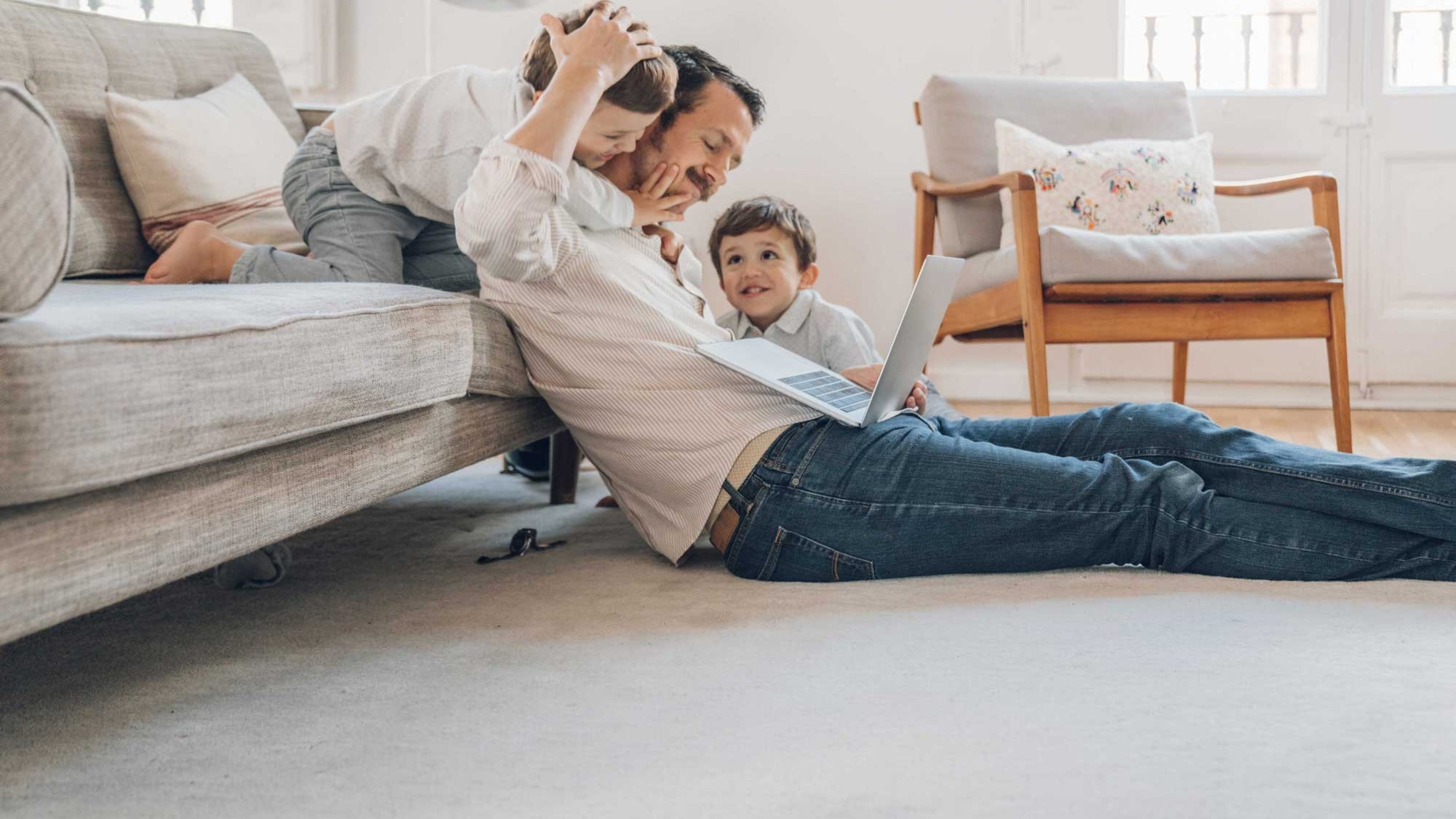 Le père est assis avec ses deux enfants dans le salon et se renseigne sur les hypothèques sur son ordinateur portable.
