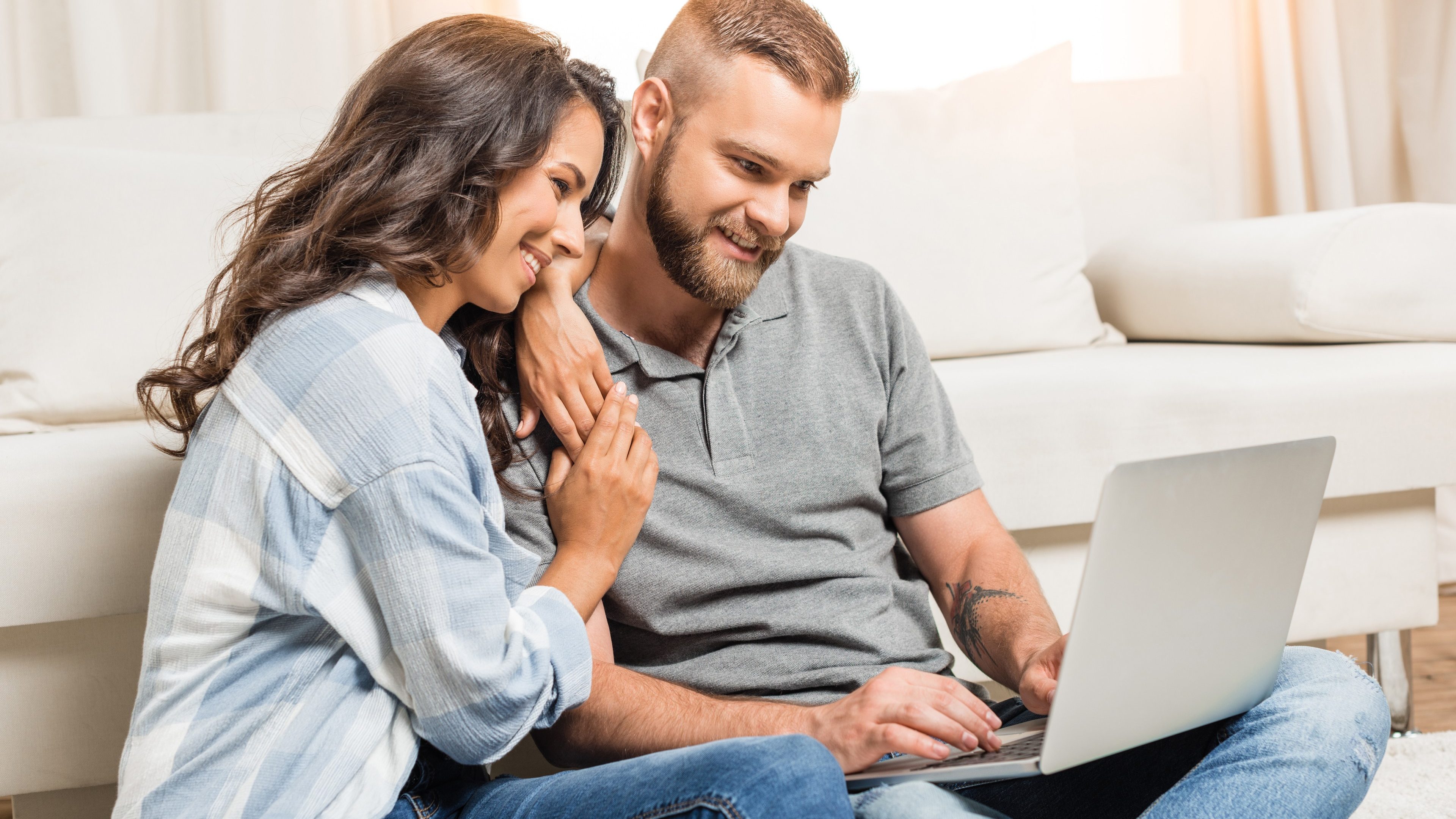 young happy couple using laptop while sitting on carpet at home