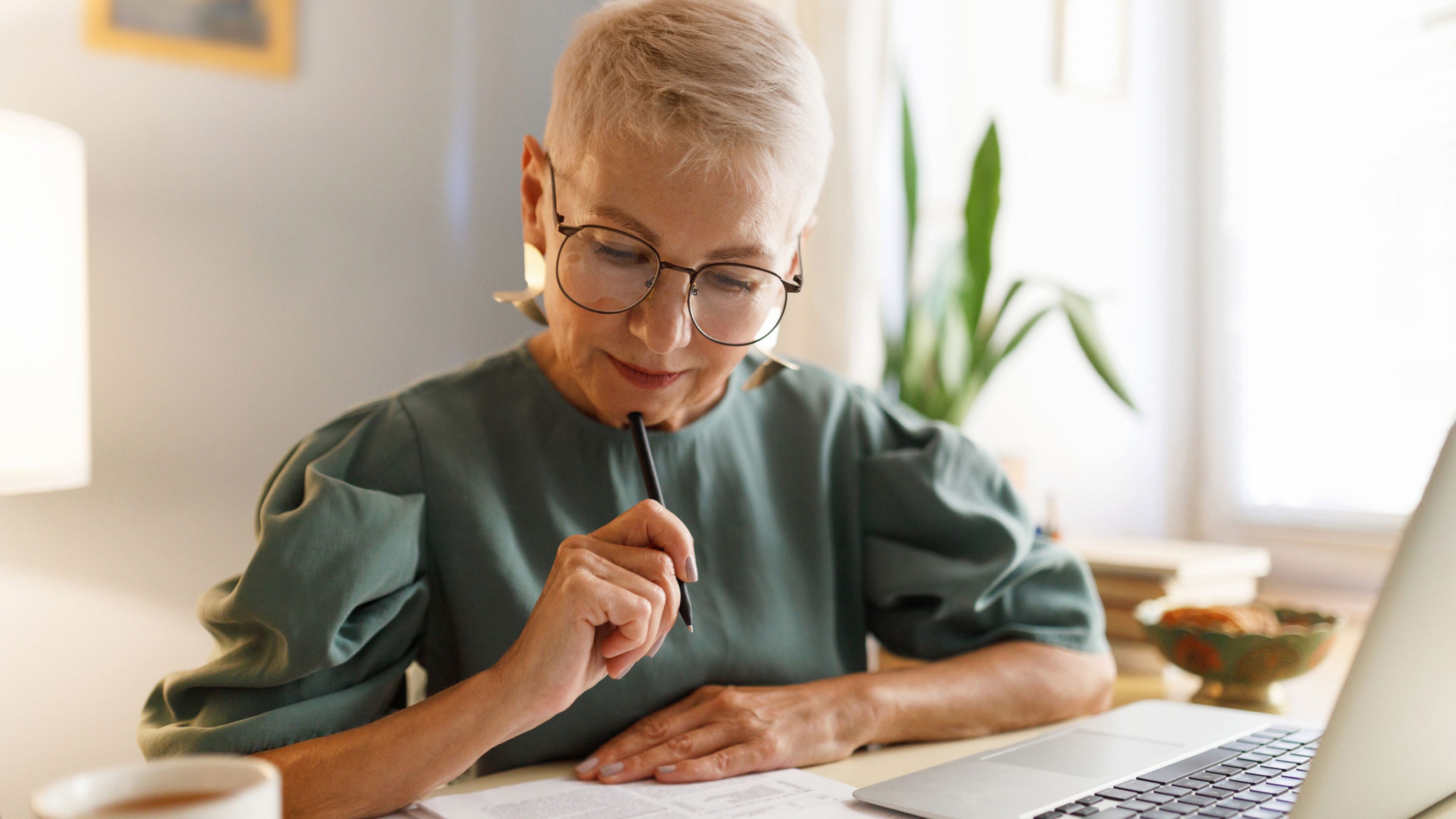 Une femme est assise à une table et signe des documents. Devant elle, se trouve un ordinateur.