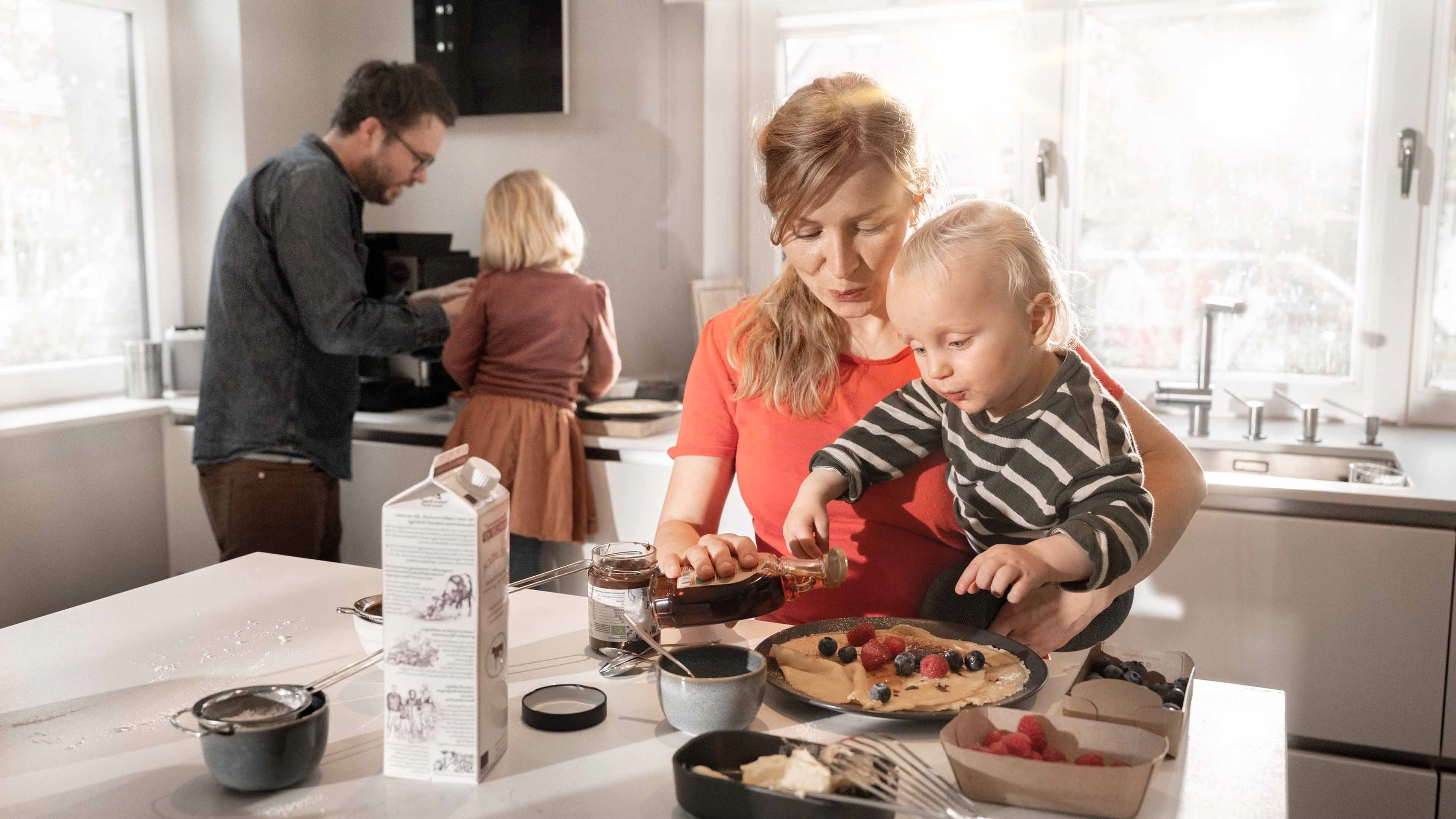La mère, avec son enfant dans les bras, sucre les crêpes.